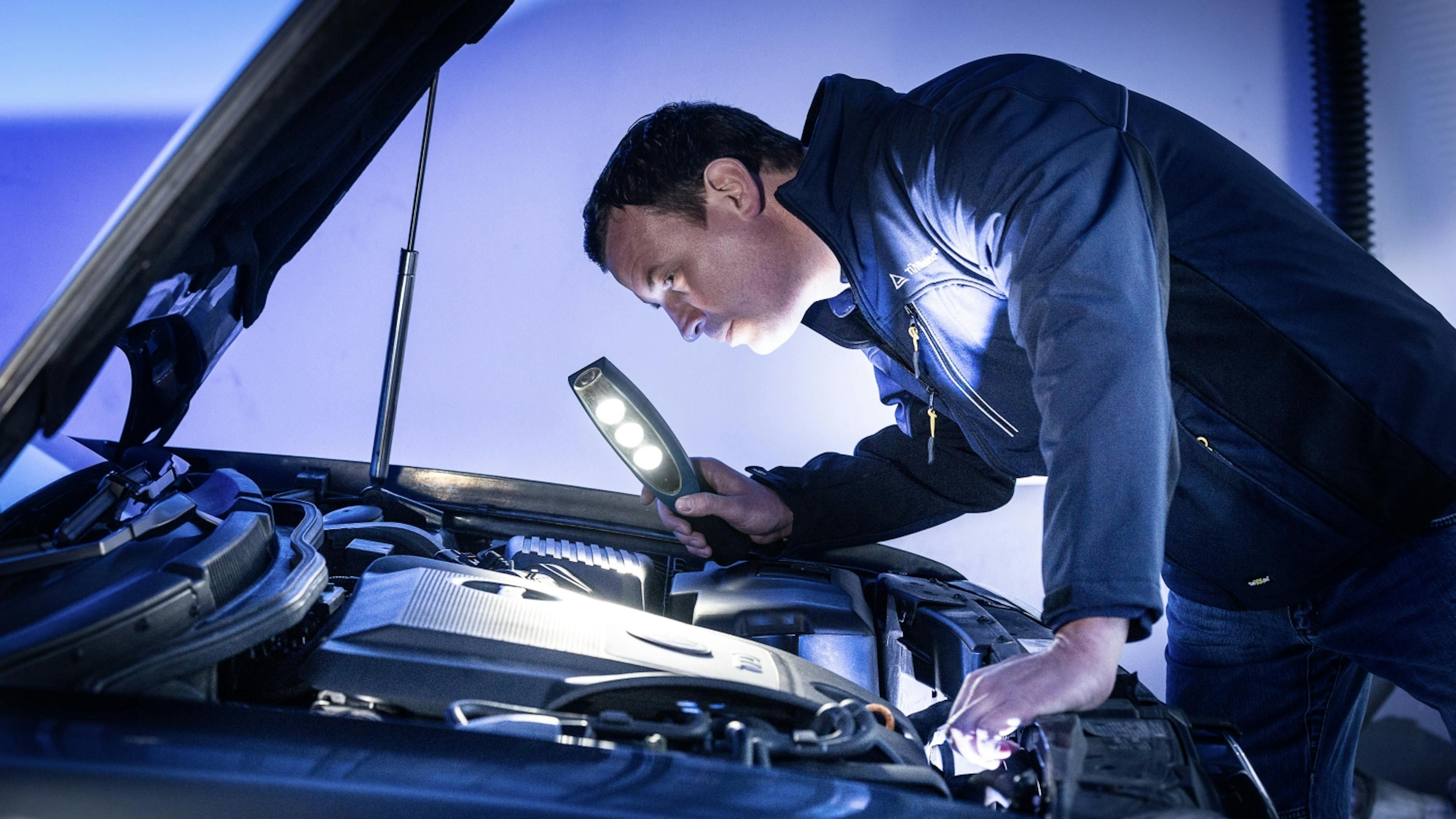A car mechanic examines the engine compartment of a car.