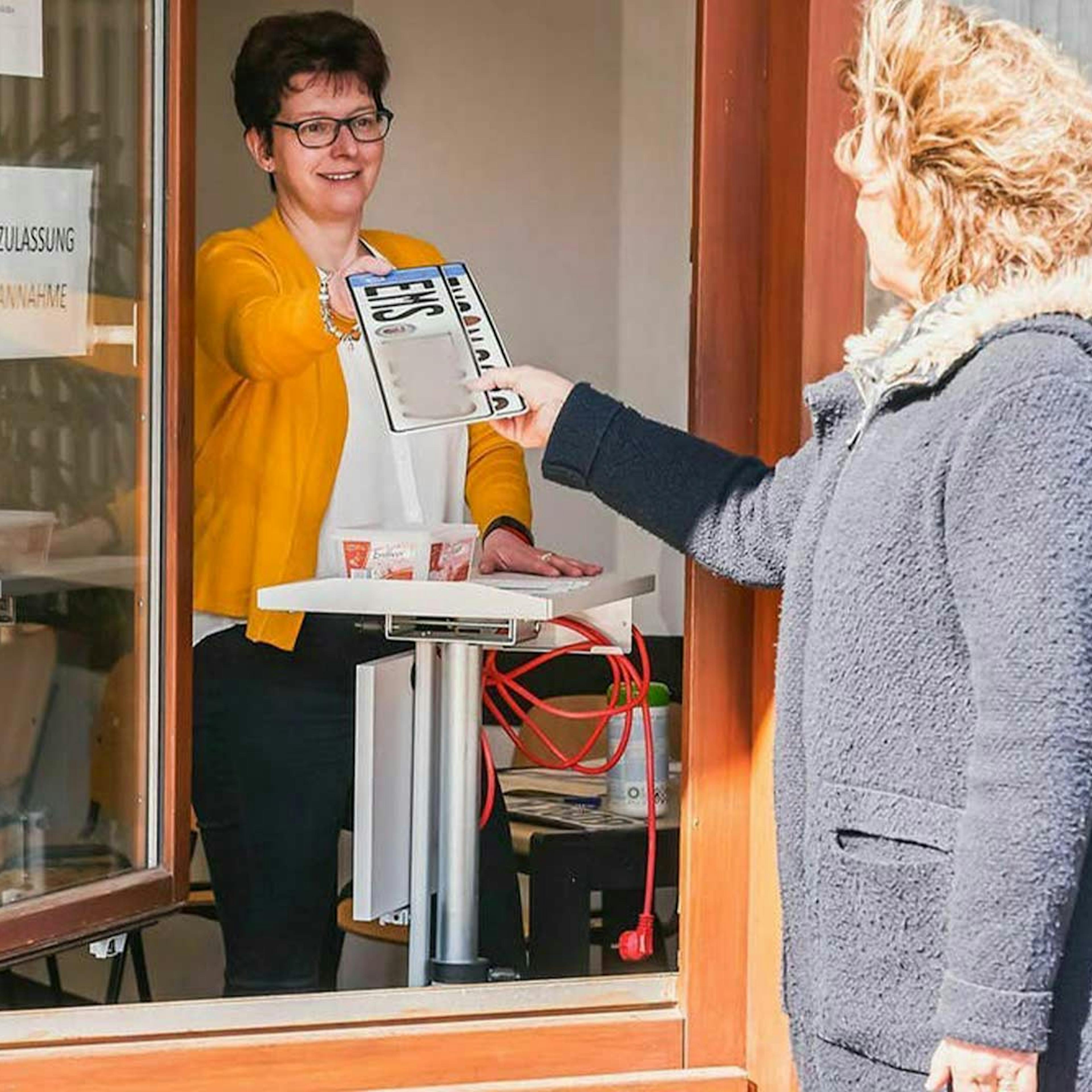 Eine Frau überreicht einer Kundin ein Wechselkennzeichen in einer Kfz-Zulassungsstelle
