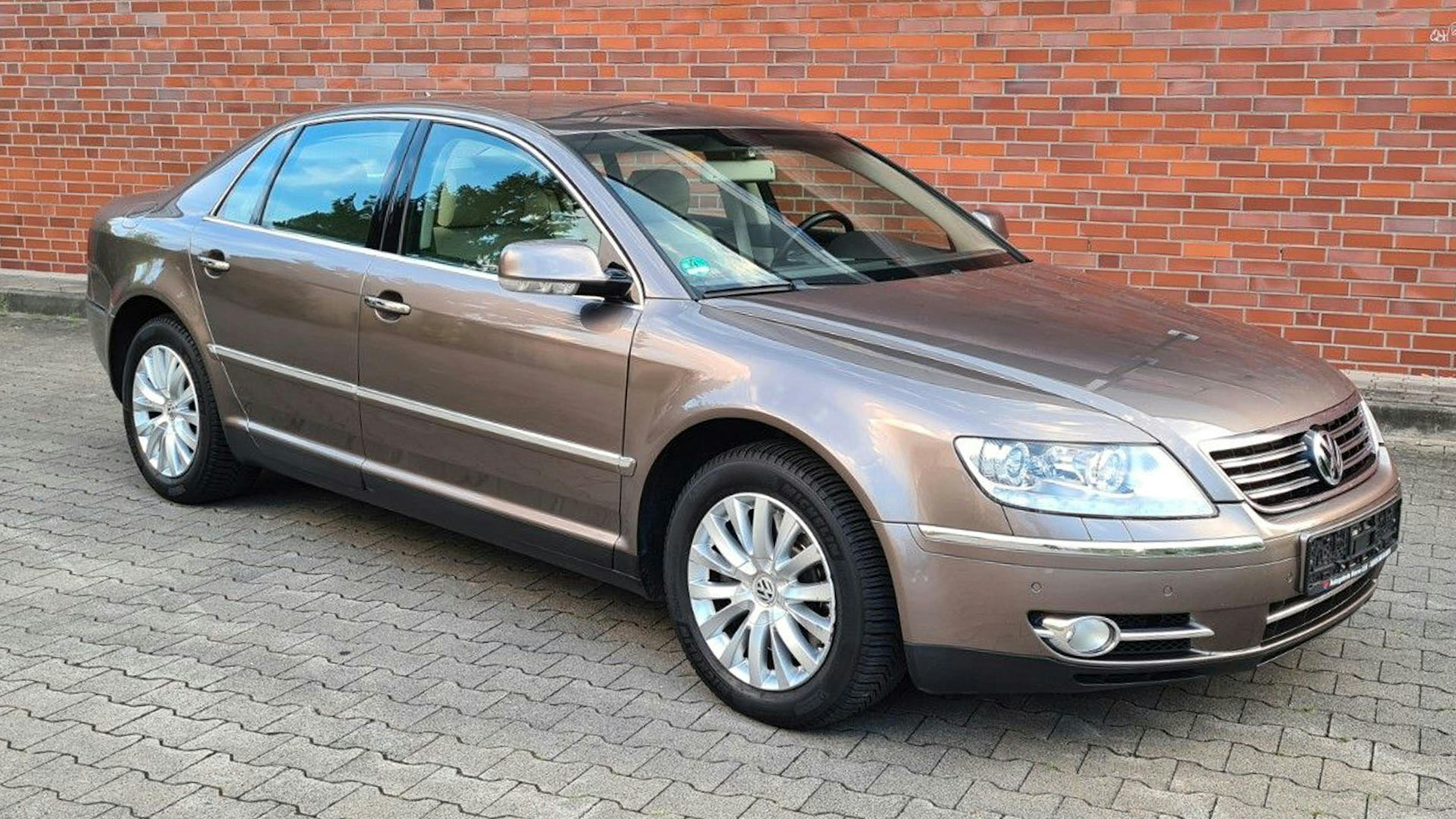 Ein metallic-brauner VW Phaeton steht vor einer Backsteinwand.