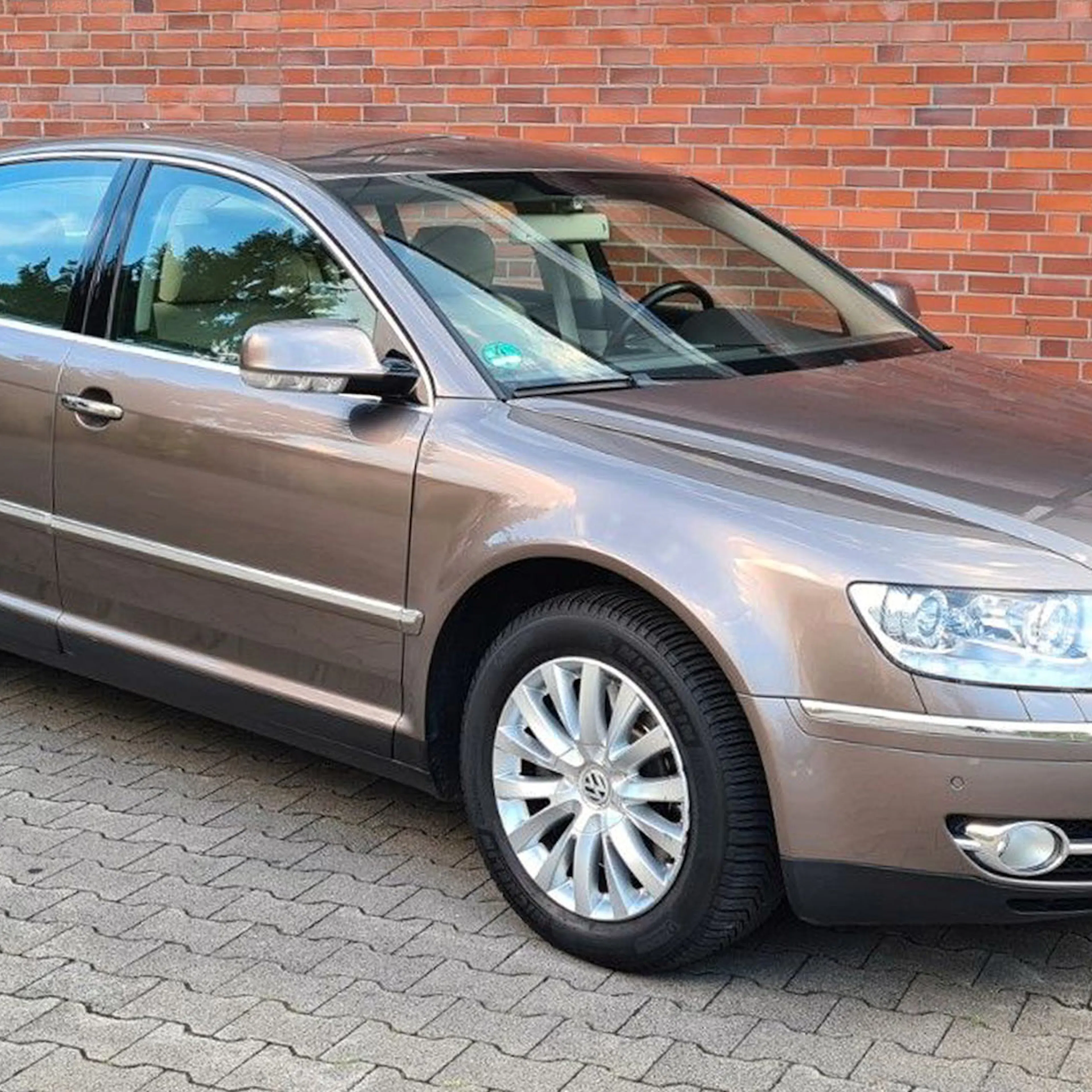 Ein metallic-brauner VW Phaeton steht vor einer Backsteinwand.