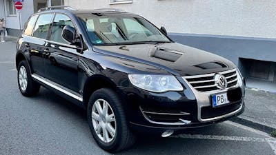 Ein schwarzer VW Touareg Geländewagen parkt vor einem Haus mit weiß-grauer Fassade.