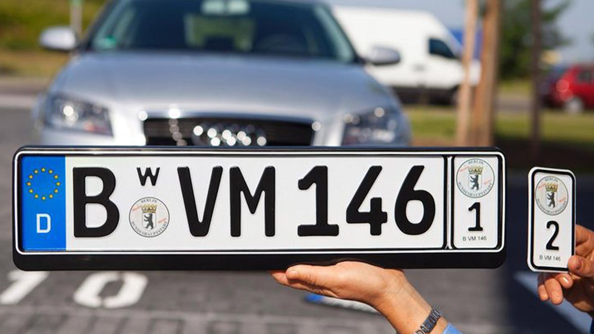Hände halten ein Wechselkennzeichen vor einem silbernen Audi