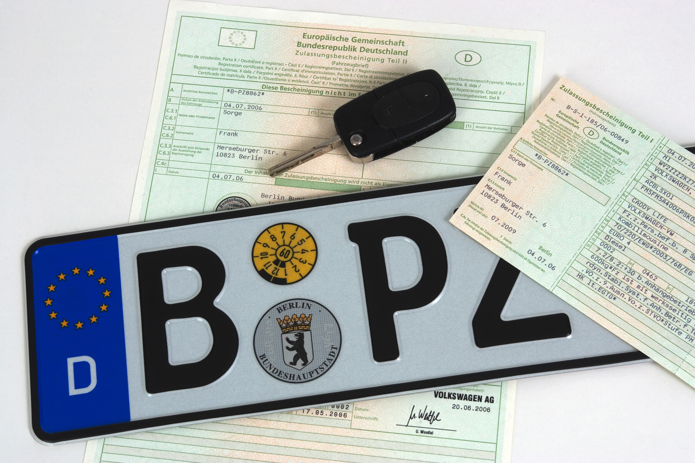 Ein Nummernschild liegt auf einem Fahrzeugbrief (Zulassungsbescheinigung Teil II). Darauf: ein Fahrzeugschein (Zulassungsbescheinigung Teil I).