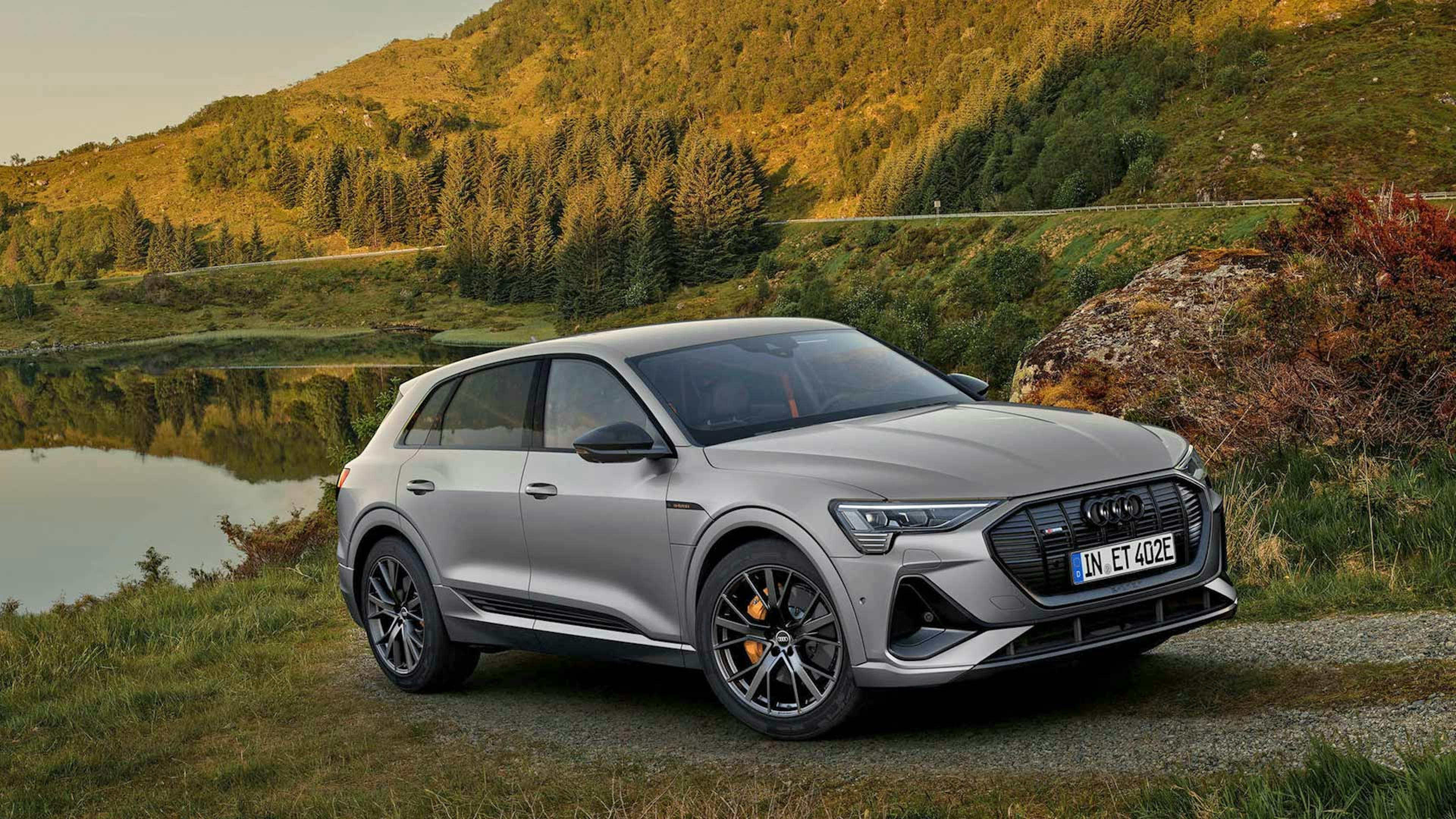 Ein graues Audi-e-tron-Sportback-Elektroauto mit Allradantrieb steht am Ufer eines Sees.