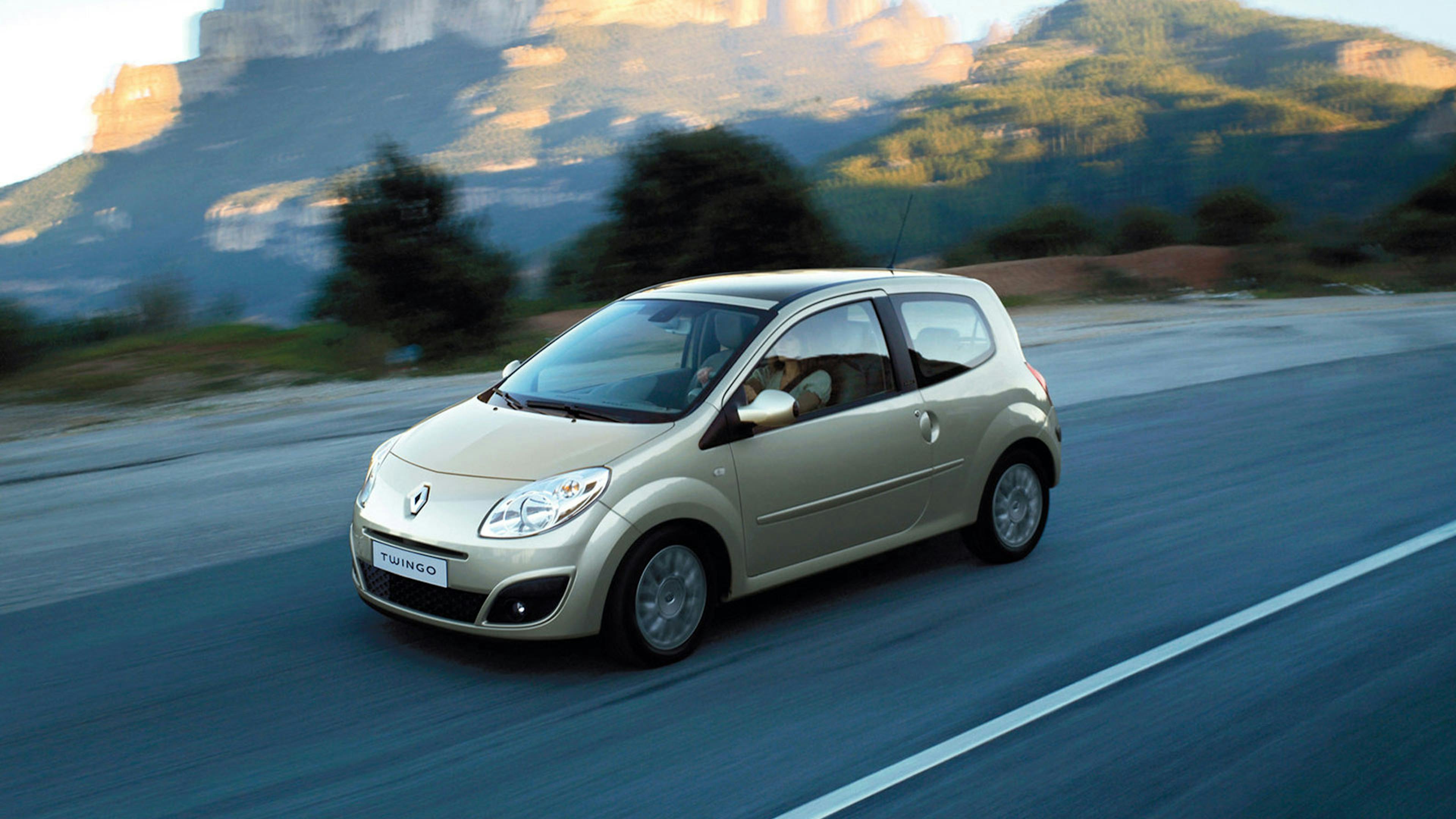 Ein silberner Renault Twingo Kleinstwagen fährt eine Landstraße entlang.