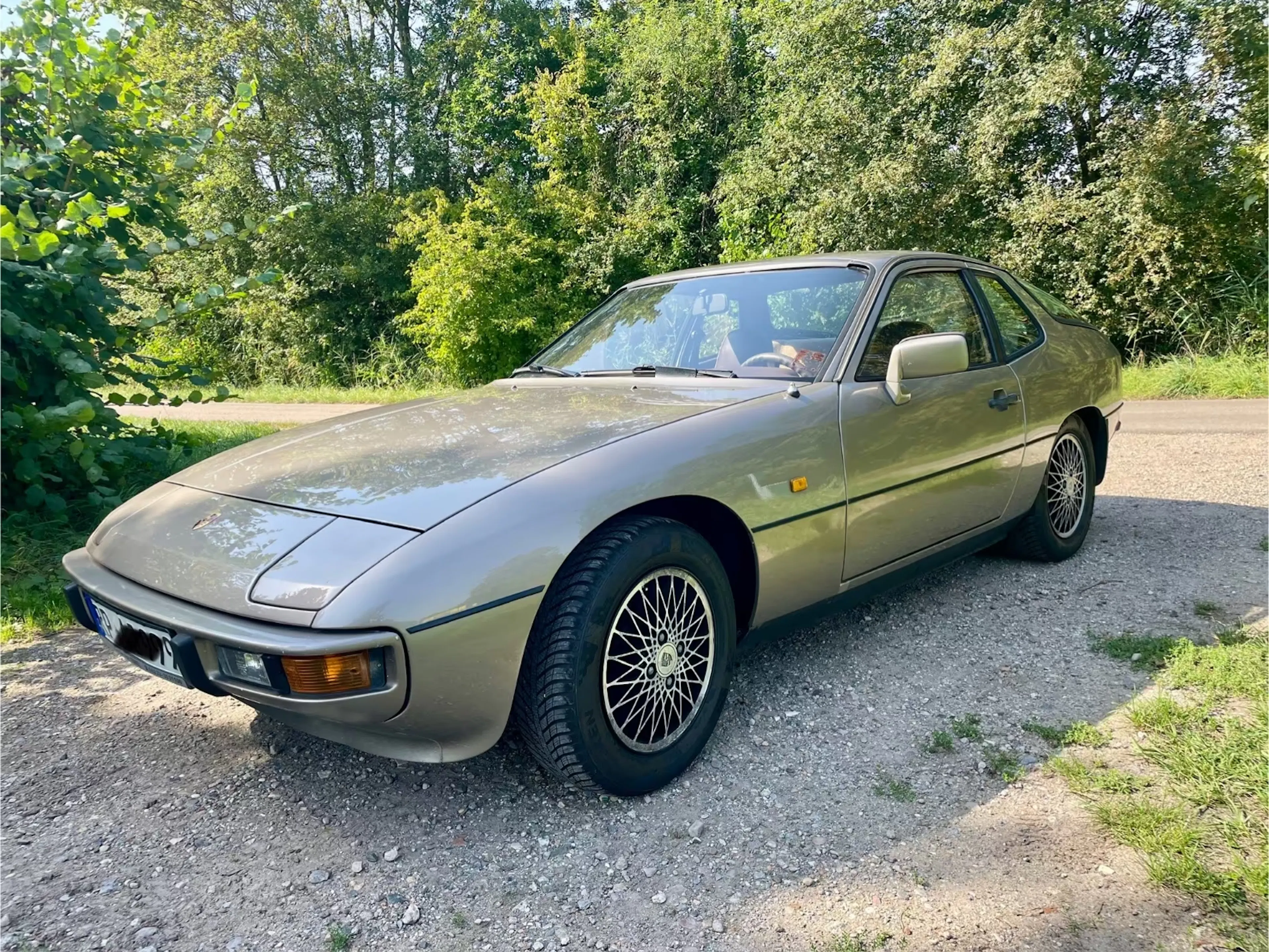 Ein goldbrauner Porsche 924 steht auf einem Feldweg.