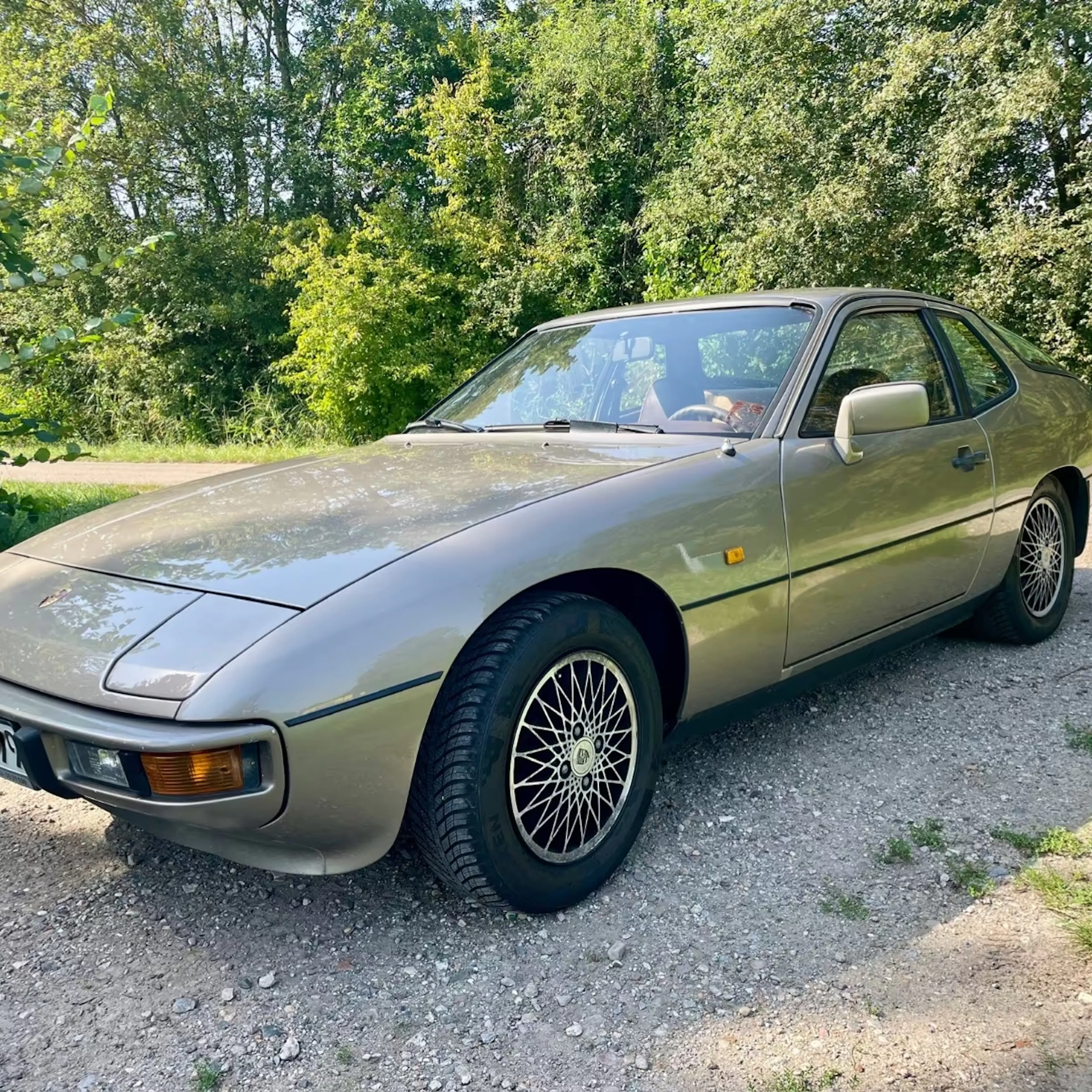 Ein goldbrauner Porsche 924 steht auf einem Feldweg.
