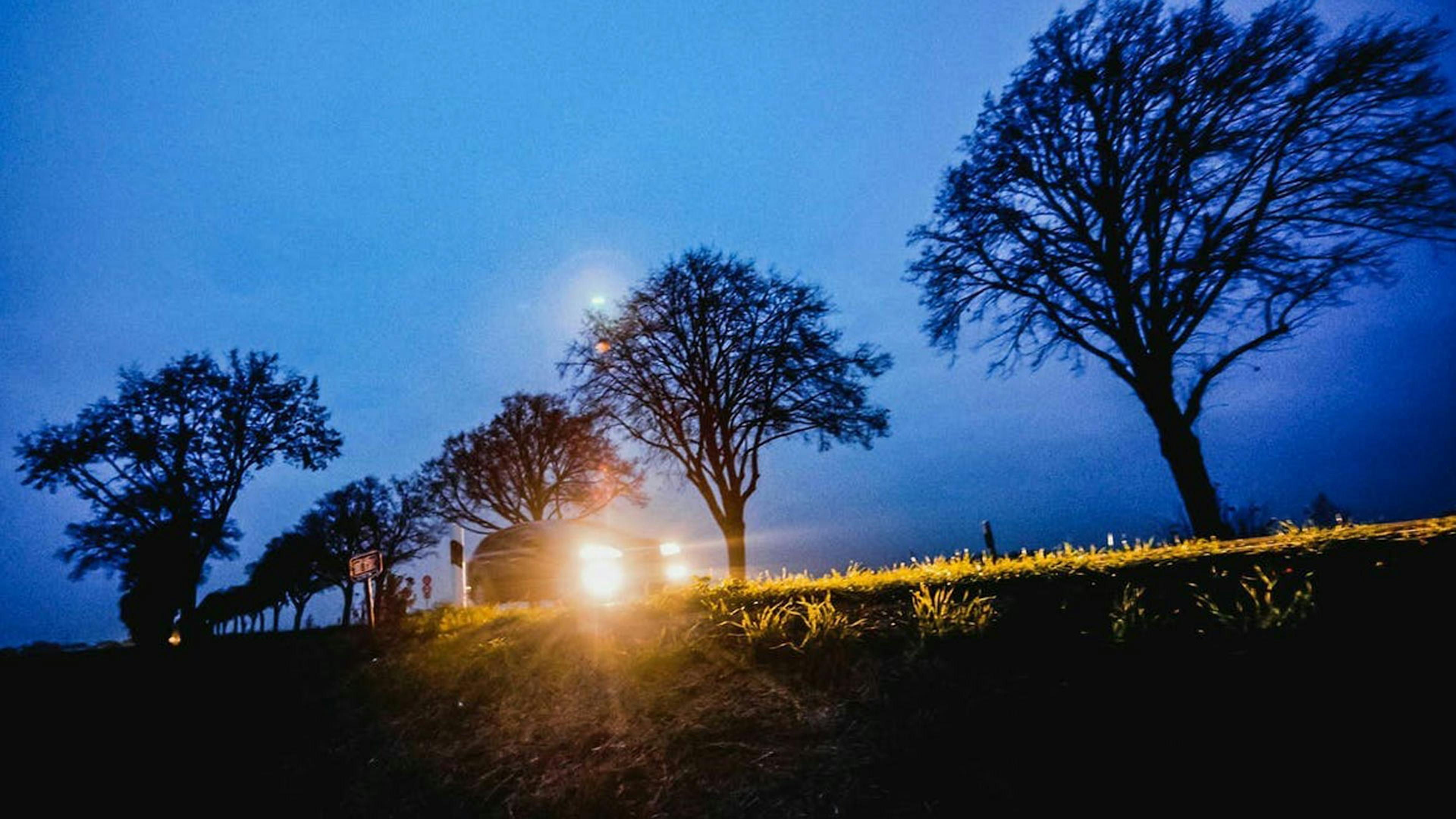 Ein Auto mit eingeschaltetem Scheinwerfer fährt nachts eine Landstraße entlang.