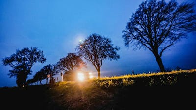 Ein Auto mit eingeschaltetem Scheinwerfer fährt nachts eine Landstraße entlang.