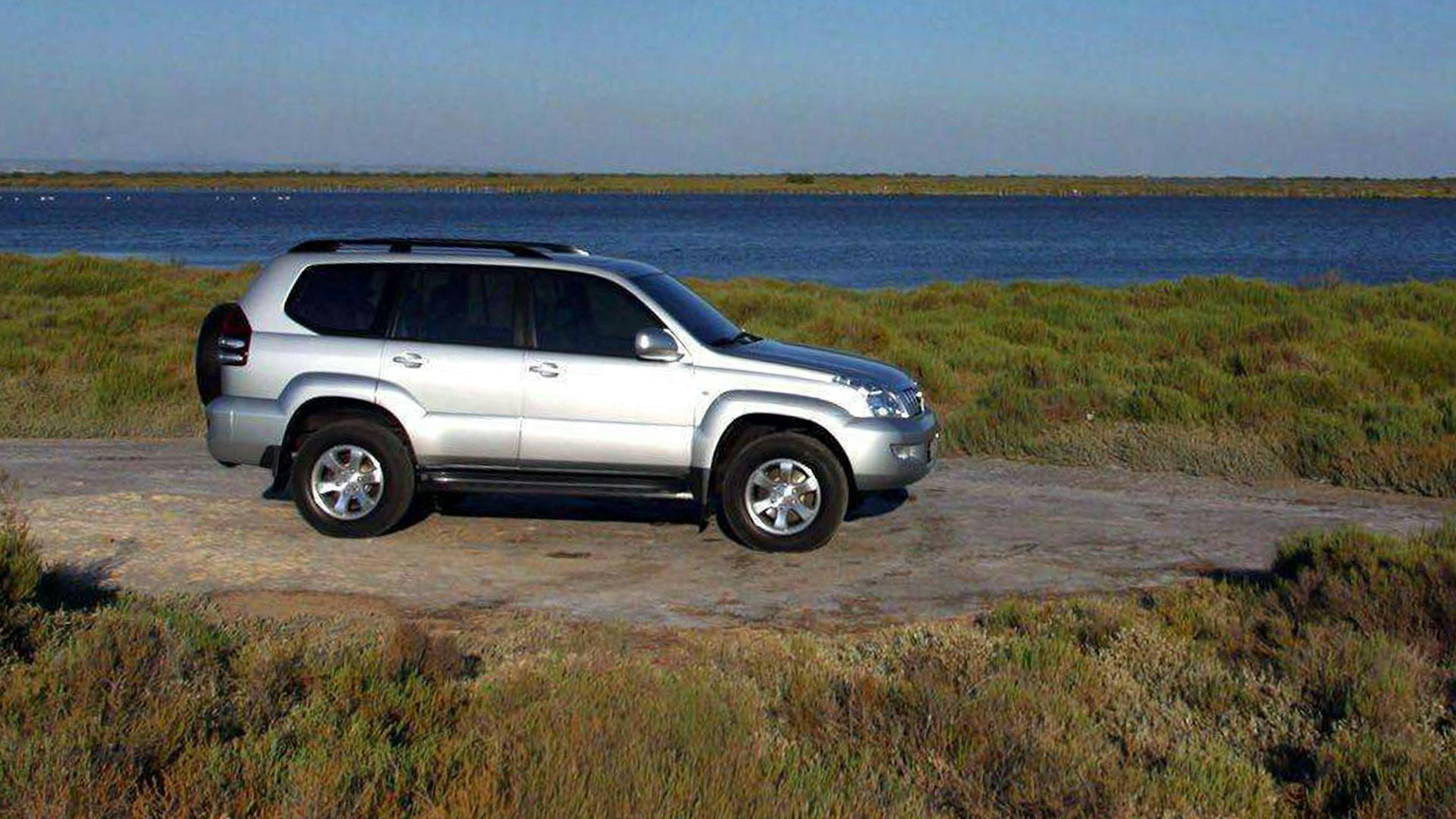 Ein silberner Toyota Land Cruiser Geländewagen steht auf einer Anhöhe vor einem Gewässer.