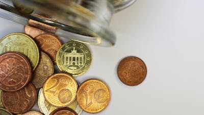 Detailaufnahme eines auf der Seite liegenden Glasbehälters, aus dem verschiedene Euromünzen herausgefallen sind