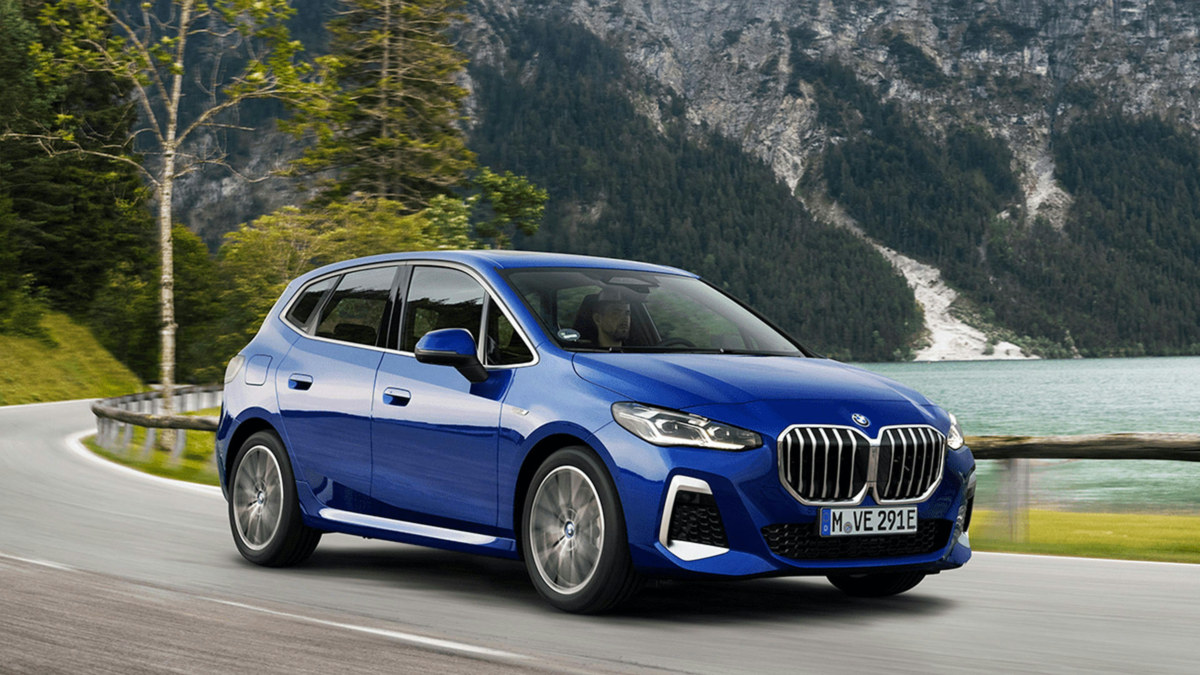 Ein blauer BMW 2er Active Tourer PHEV fährt an einem Bergsee vorbei.