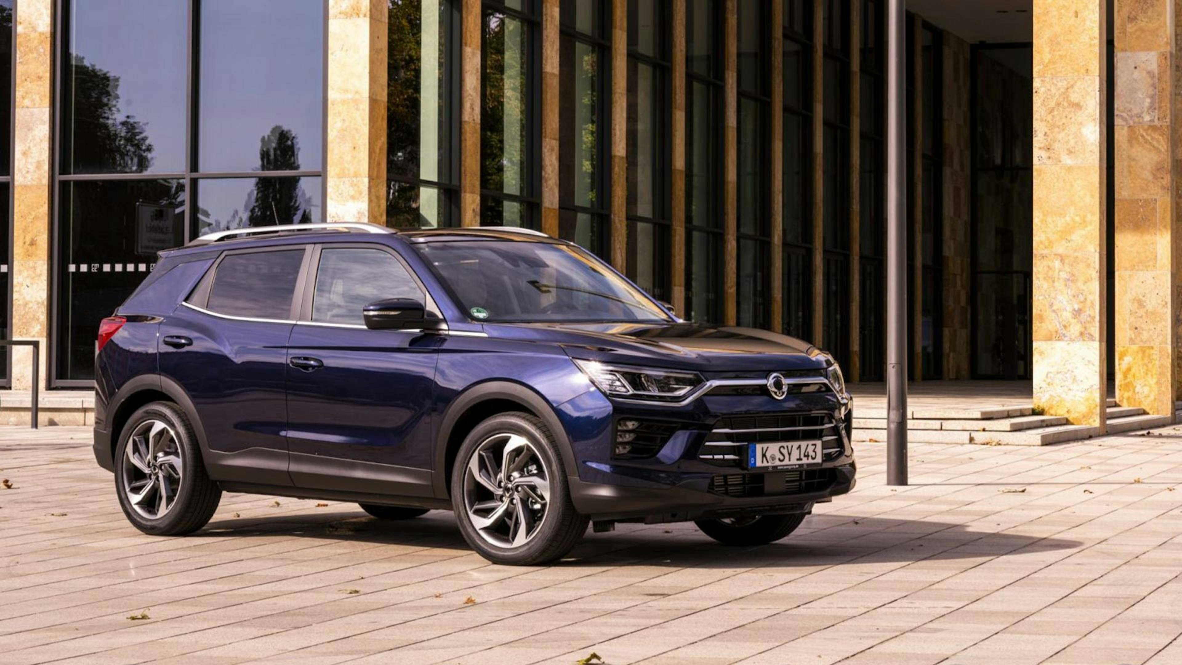 Ein dunkelblauer SsangYong Korando steht vor einem Gebäude mit goldener Fassade.