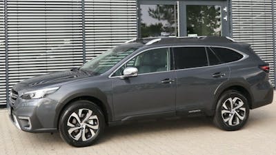 Ein grauer Subaru Outback steht vor einem Gebäude mit Fensterfront.