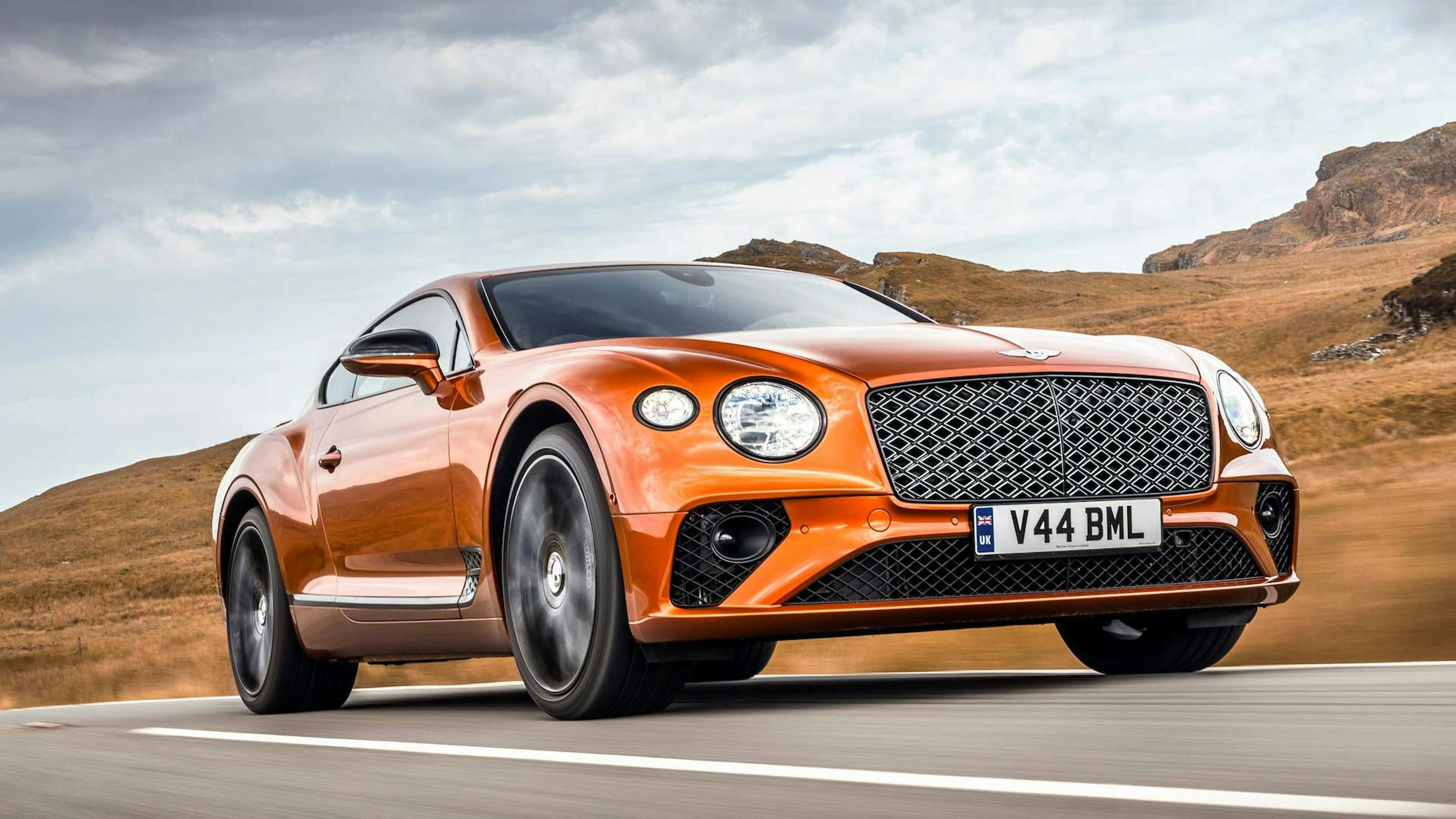 Ein orangefarbener Bentley Continental GT fährt durch eine karge Landschaft.