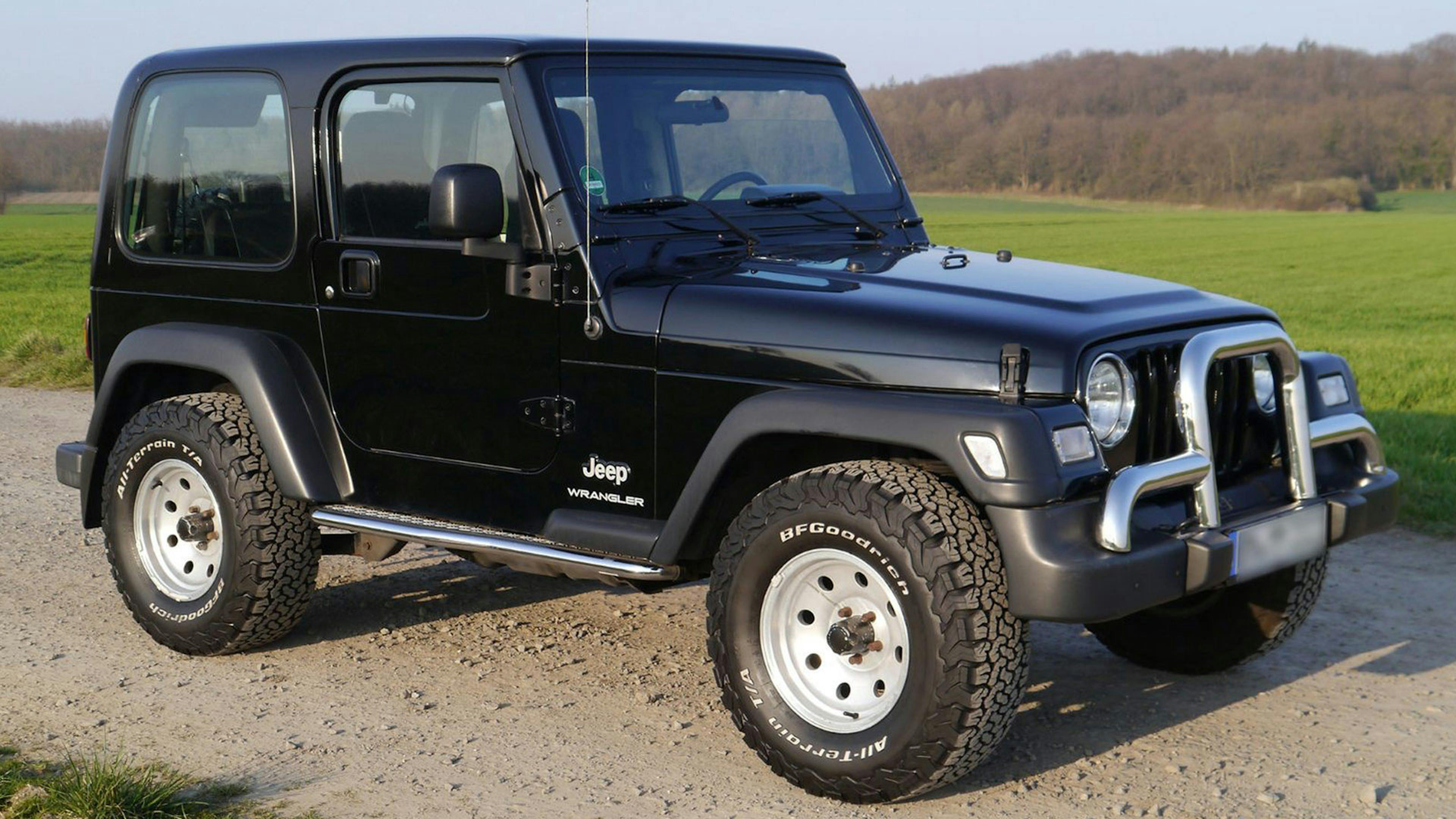 Ein schwarzer Jeep Wrangler Geländewagen steht auf einem Feldweg.