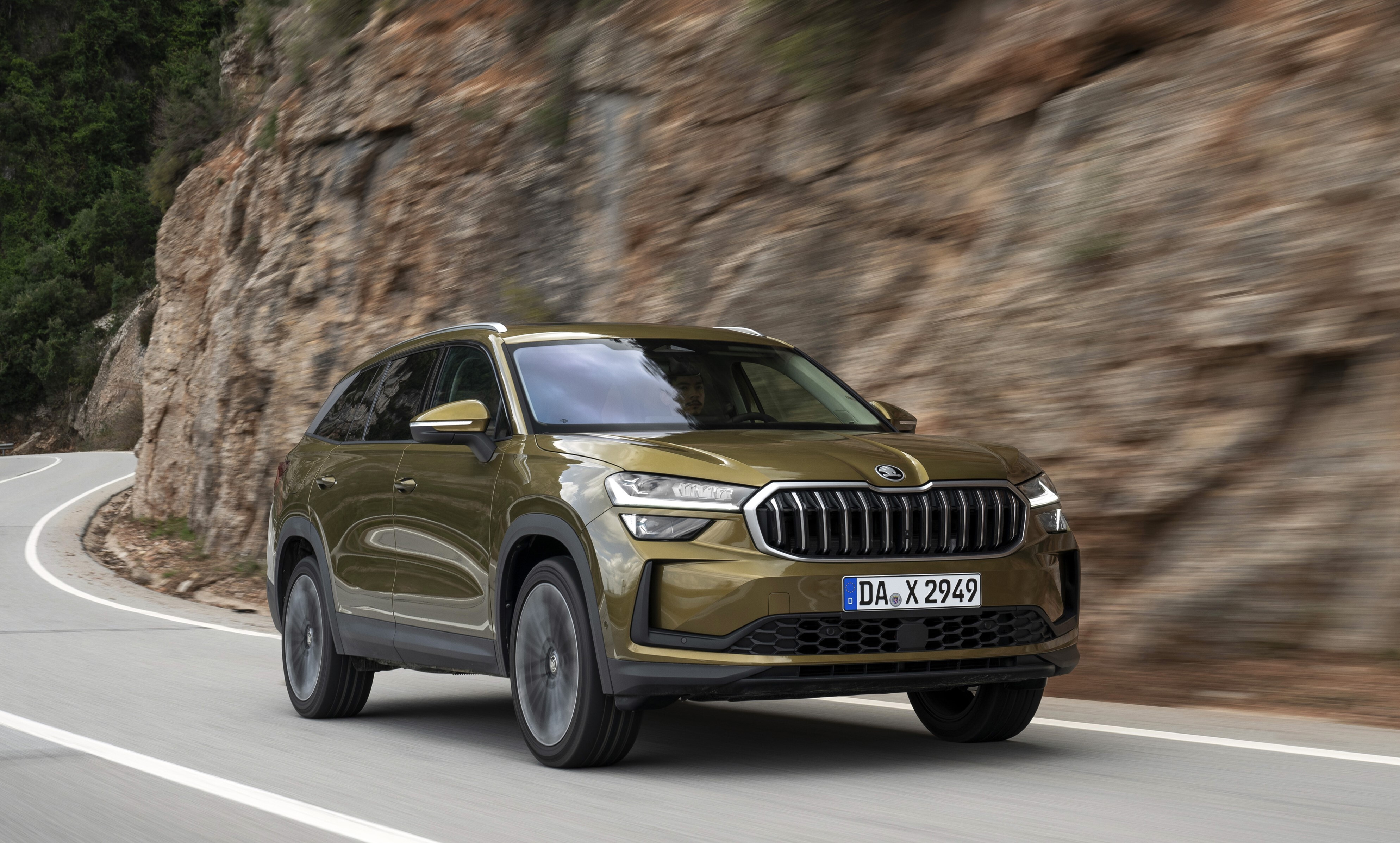 Olivgrüner Škoda Kodiaq fährt seitlich von vorn gesehen an einer Felswand entlang.