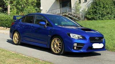 Ein blauer Subaru Impreza WRX STI steht vor einem hellen Gebäude