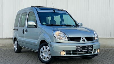 Ein blau-grauer Renault Kangoo steht vor einem grauen Gebäude.
