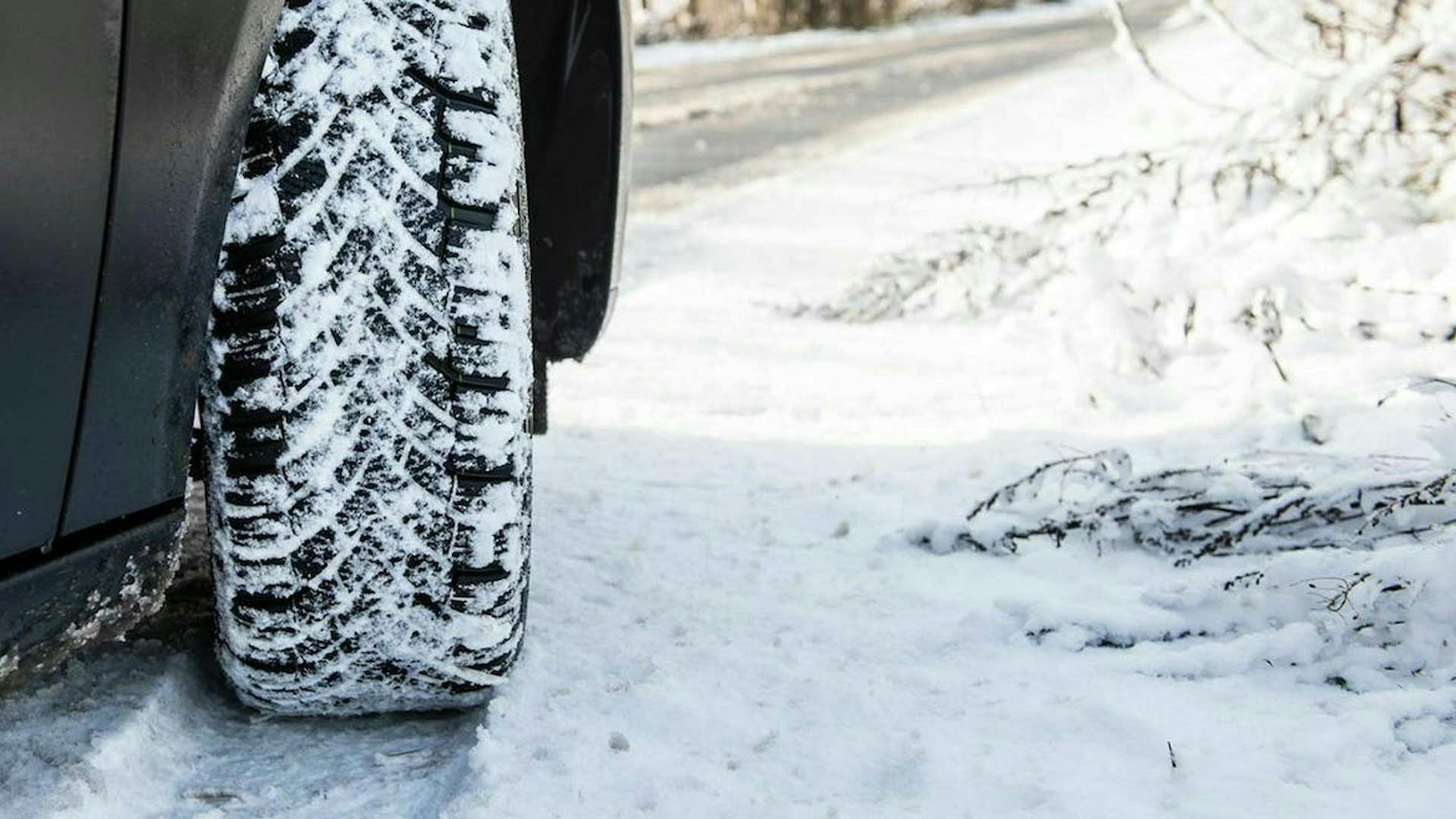 Nahaufnahme des rechten Vorderrades eines Pkw mit Winterreifen im Schnee.