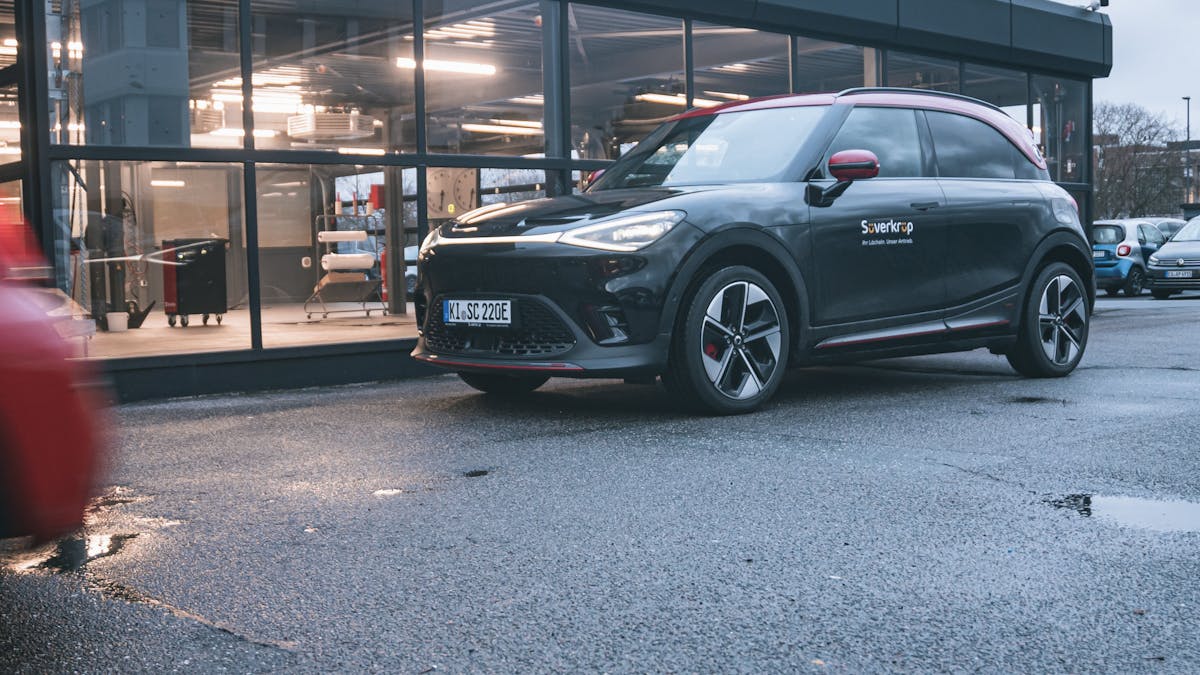 Ein schwarz-roter Smart #1 Brabus parkt vor einer beleuchteten Halle.