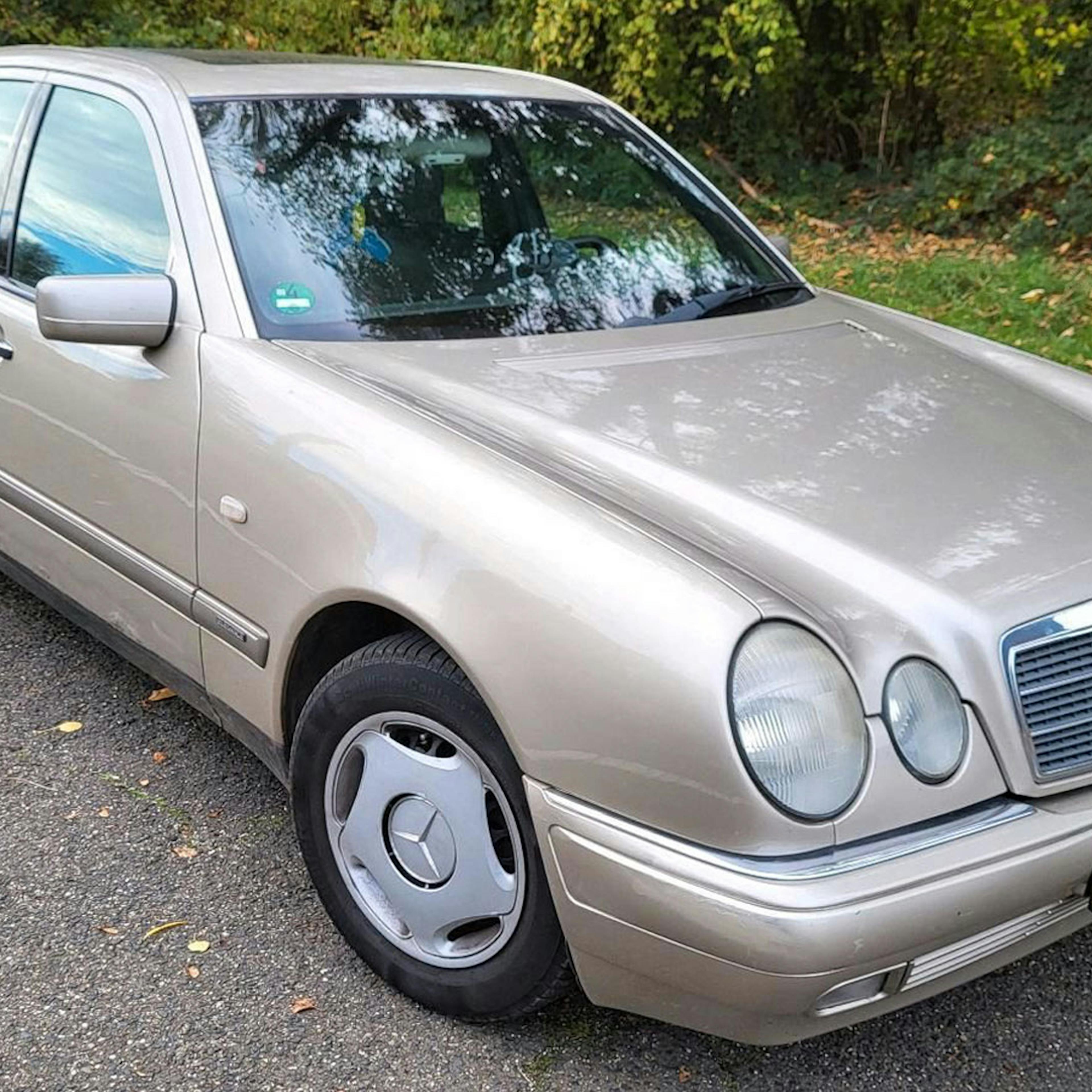 A silver Mercedes-Benz E-Class stands on a roadside with green spaces in the background.