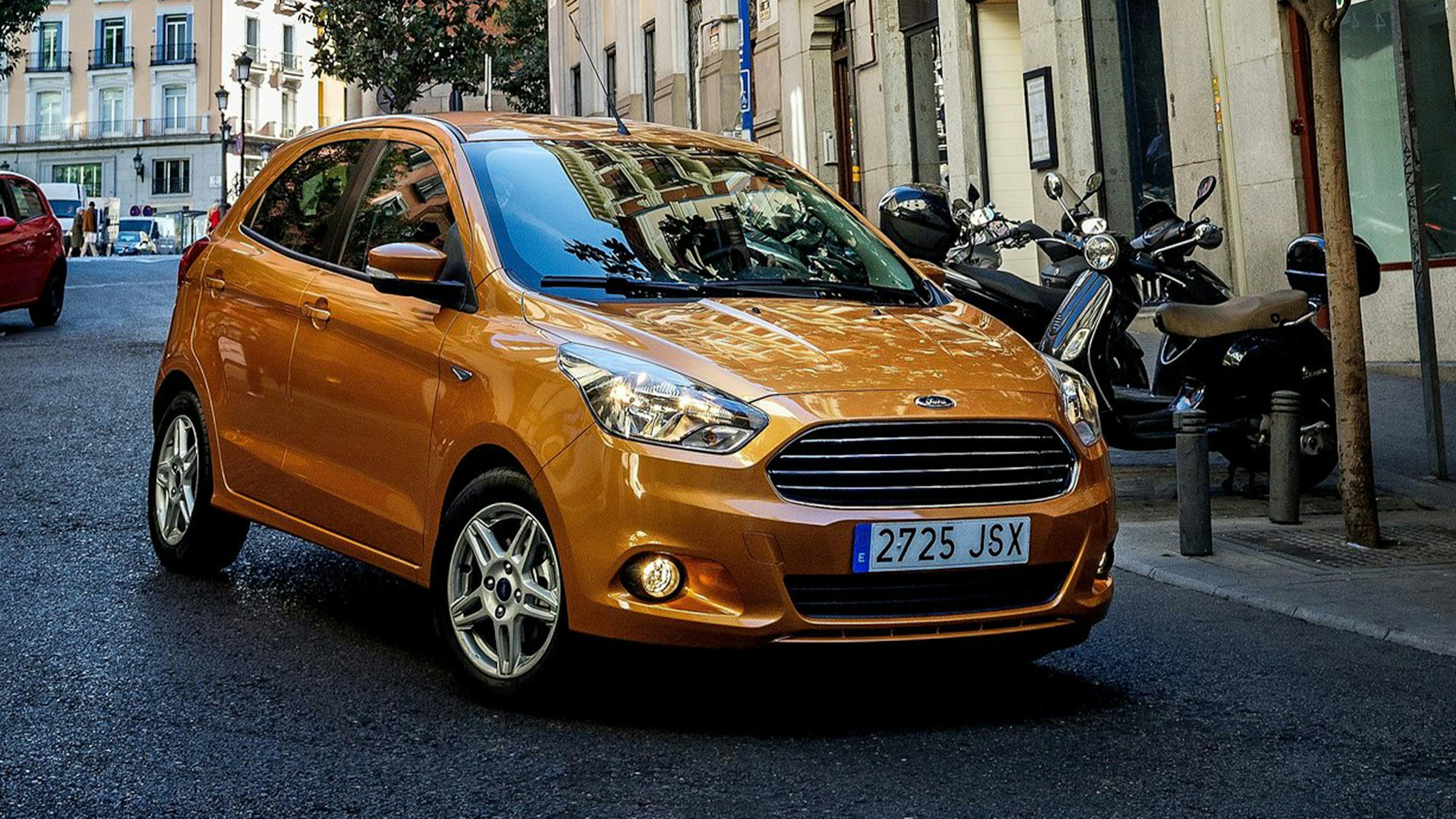 Ein goldener Ford Ka+ Kleinstwagen fährt durch eine urbane Kulisse.