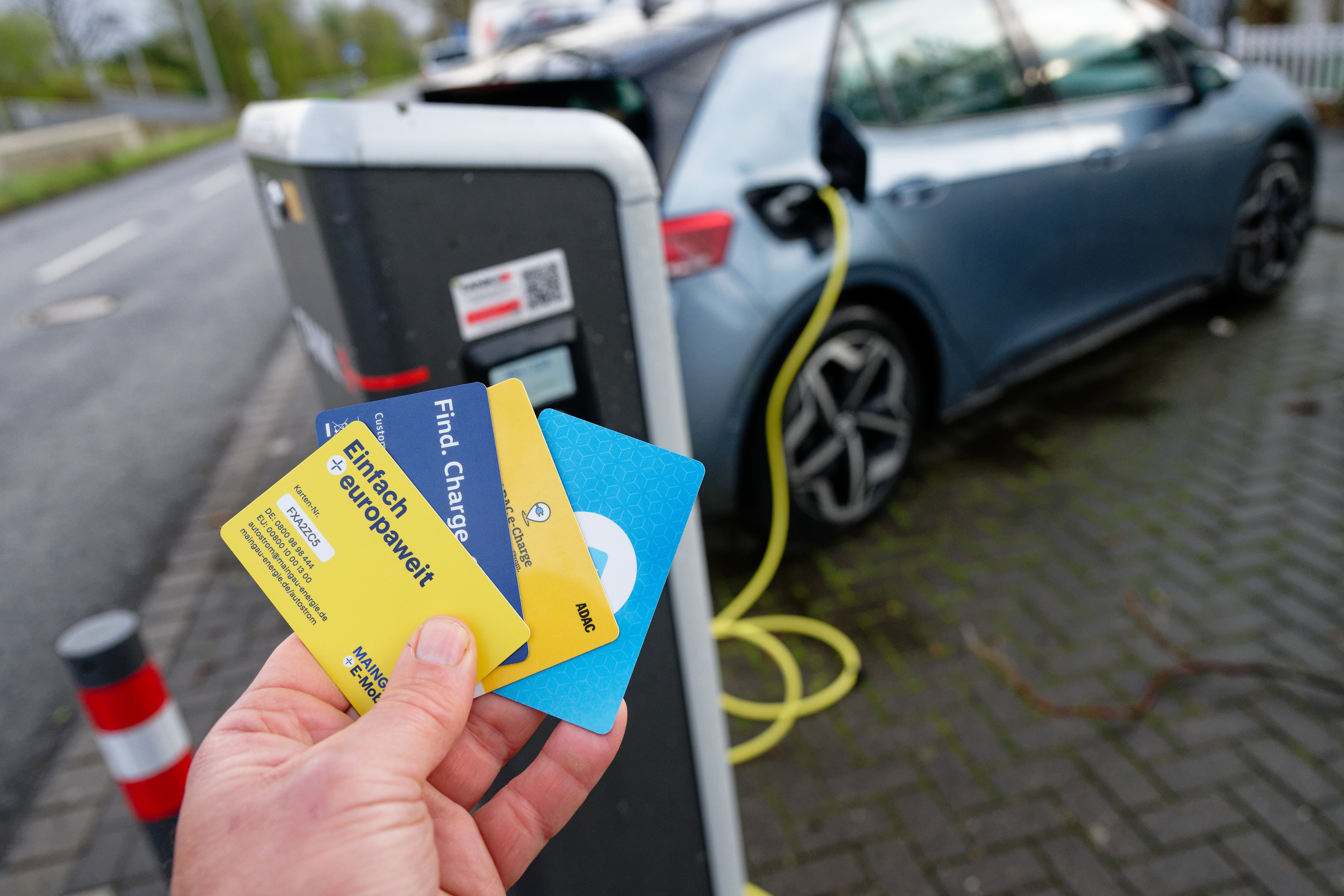 E-Auto beim Laden und eine Hand die verschiedene Karten hält