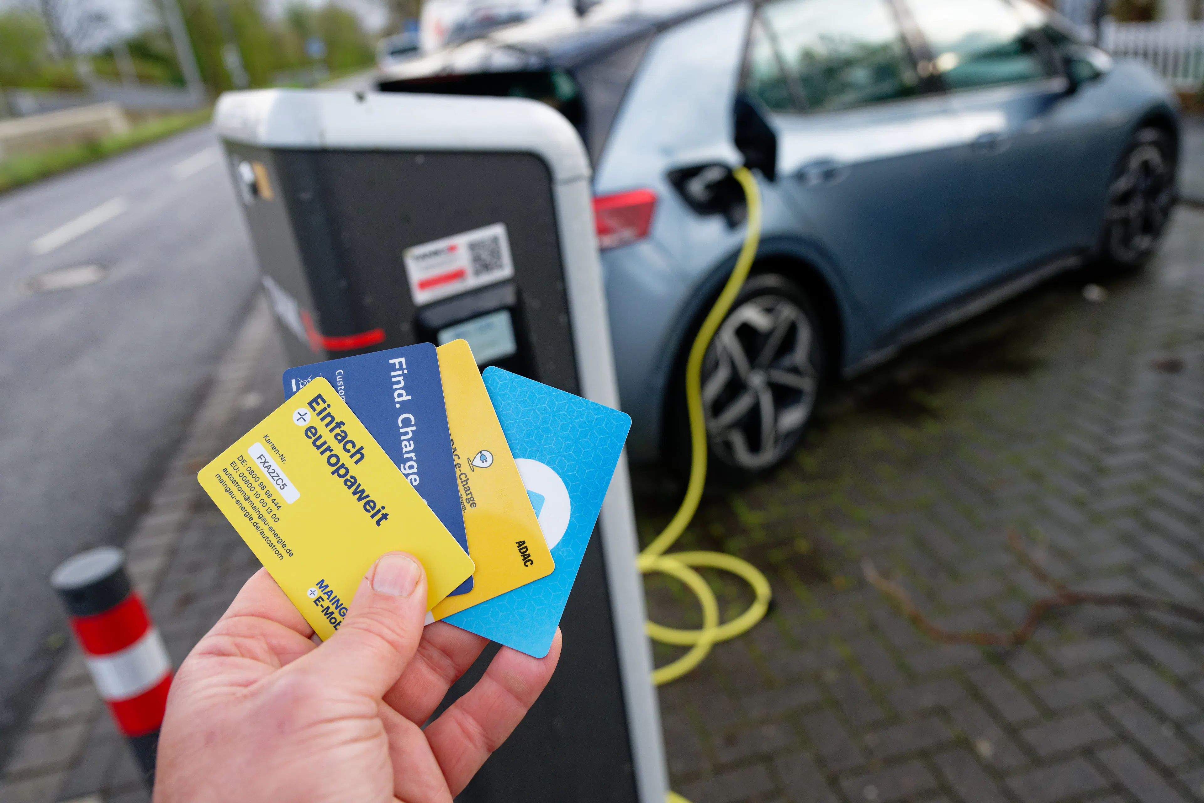 E-Auto beim Laden und eine Hand die verschiedene Karten hält