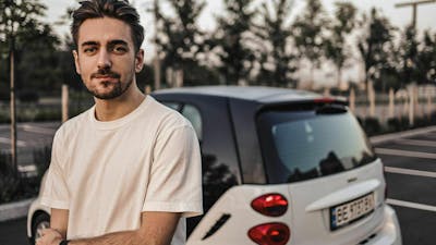 Ein junger Mann mit weißem T-Shirt steht vor einem weißen Pkw