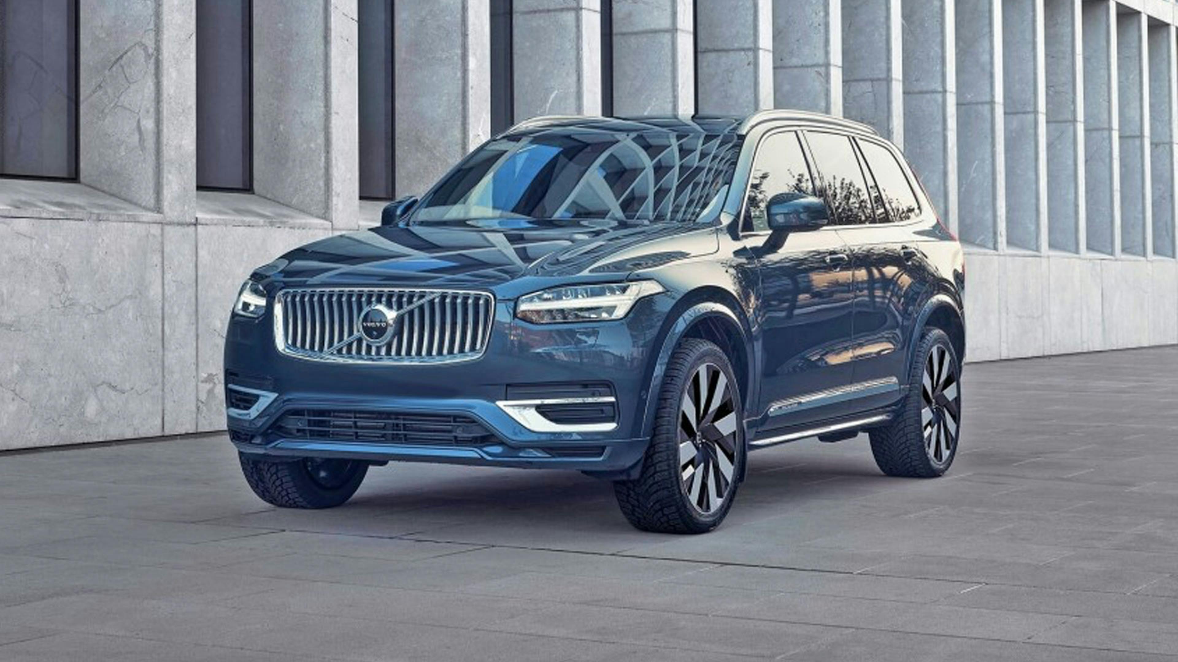 Ein dunkler Volvo XC90 T8 Recharge AWD steht vor einem grauen Gebäude.