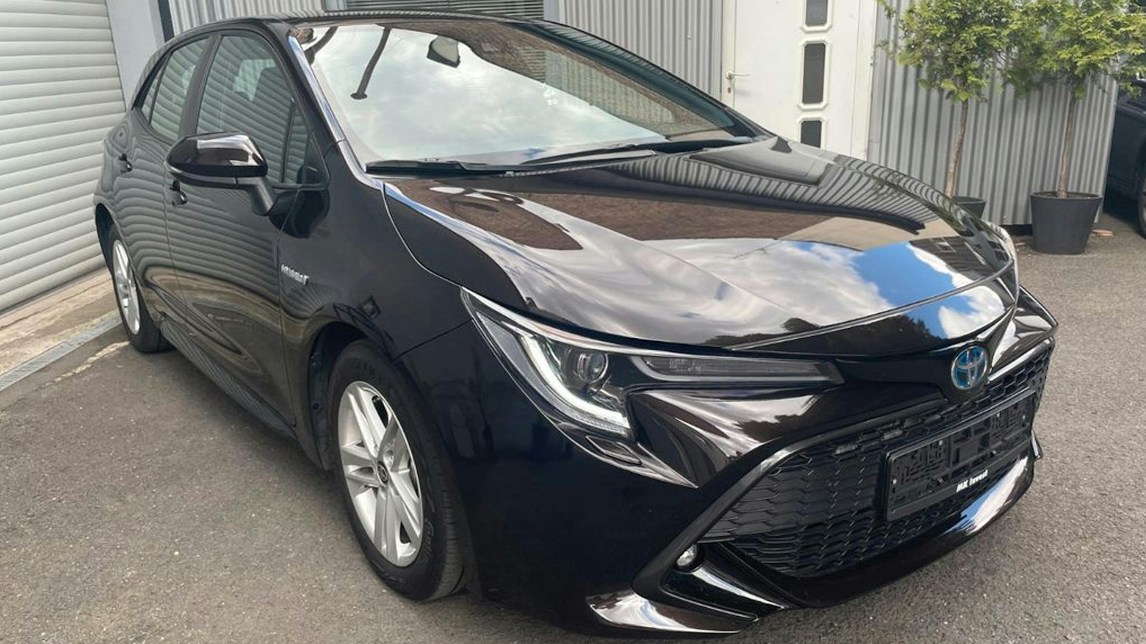 Ein schwarzer Toyota Corolla Hybrid steht vor einer Garage.