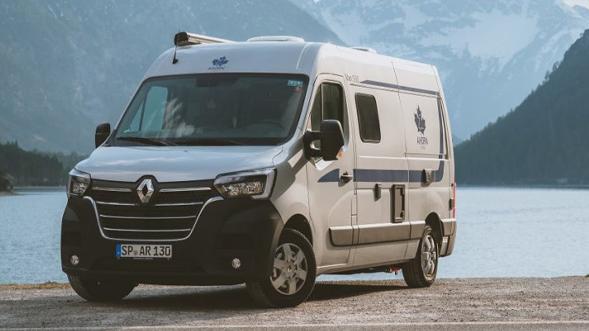 Ein weißer Ahorn Camp Van 540 Campingbus steht an einem See vor einem Bergpanorama