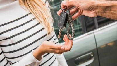 Ein Mann überreicht einer blonden Frau einen Autoschlüssel.
