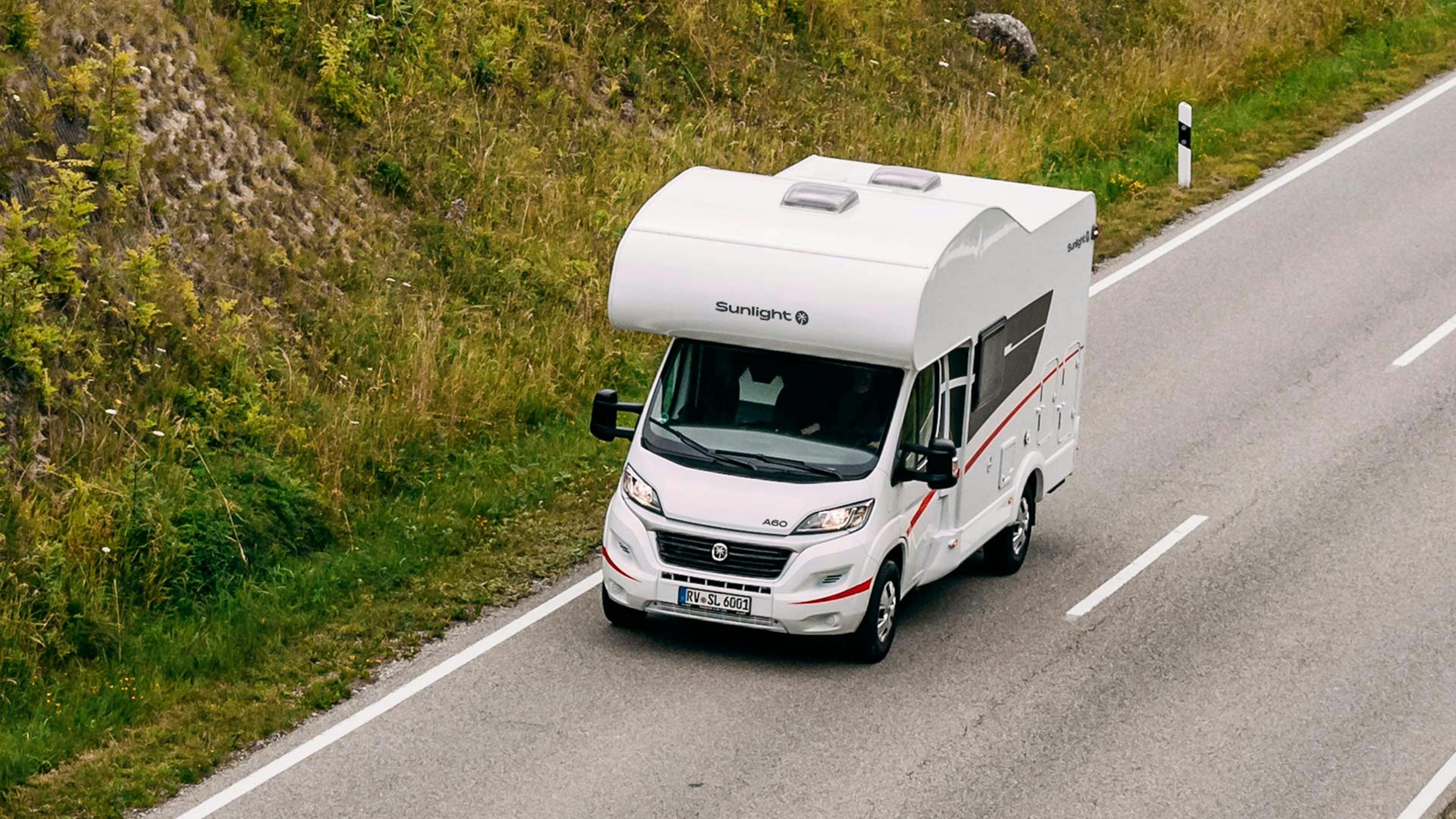 Ein Sunlight A 60 Wohnmobil mit Alkoven fährt eine Landstraße entlang.