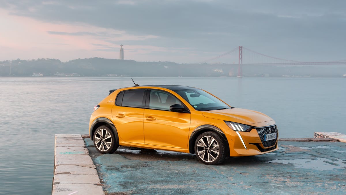 Ein gelber Peugeot 208 steht am Rand eines Gewässers.