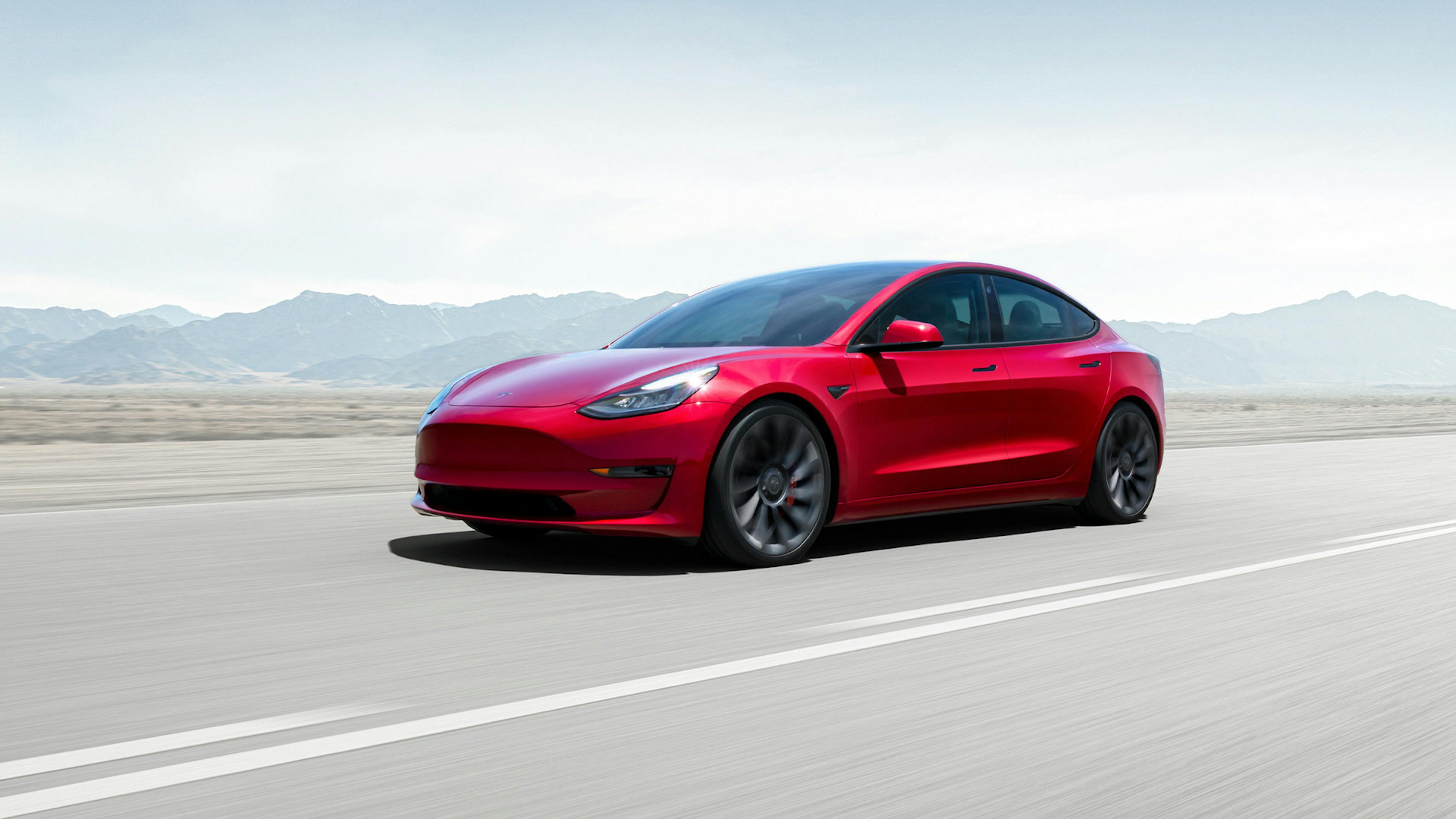 Ein rotes Tesla-Model-3-Elektroauto mit Allradantrieb fährt eine Landstraße entlang.
