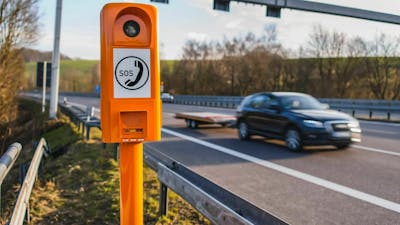 Ein schwarzer Pkw mit Anhänger fährt auf einer Autobahn an einer Notrufsäule vorbei