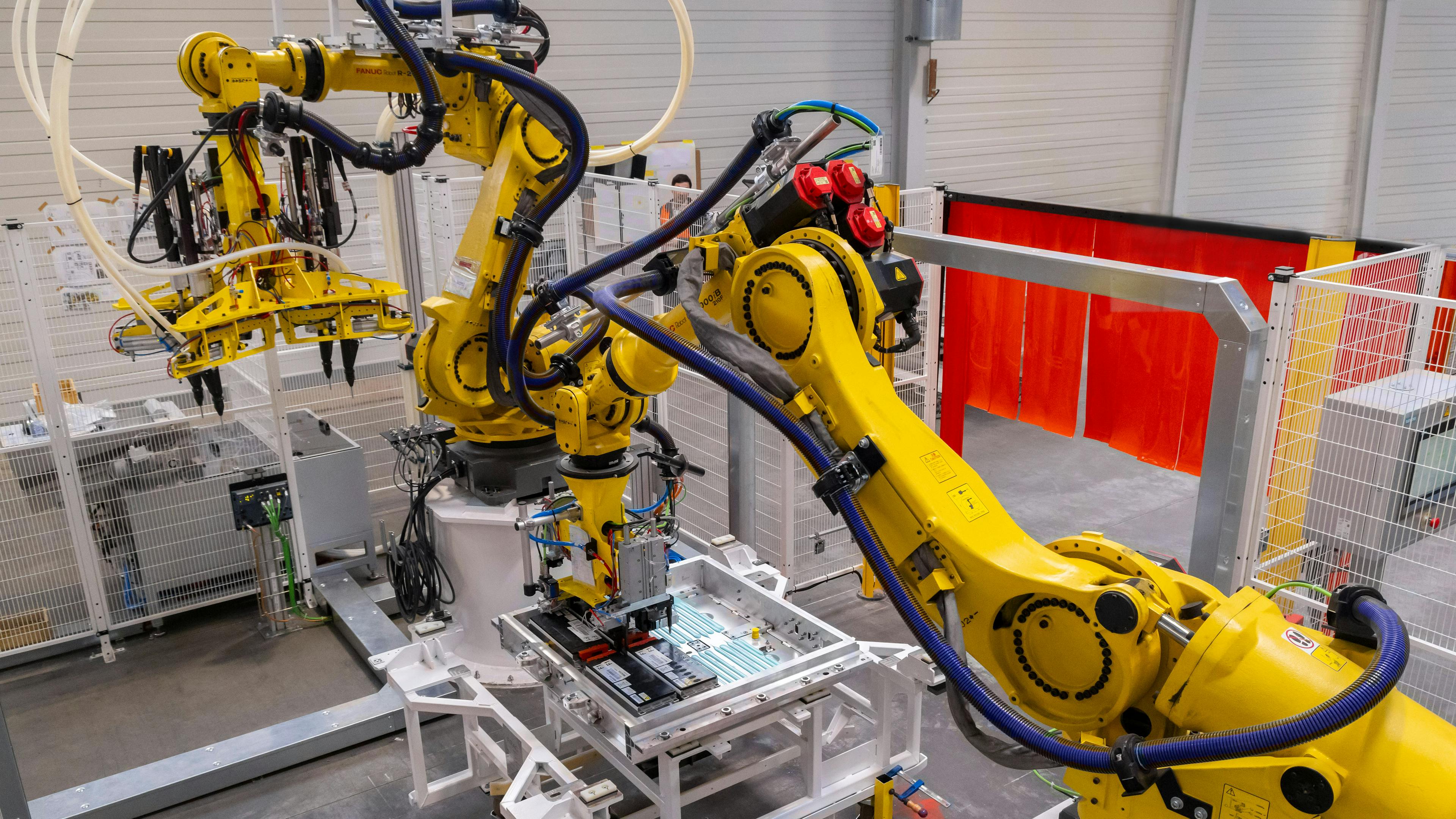 Two yellow robot arms in a factory hall.