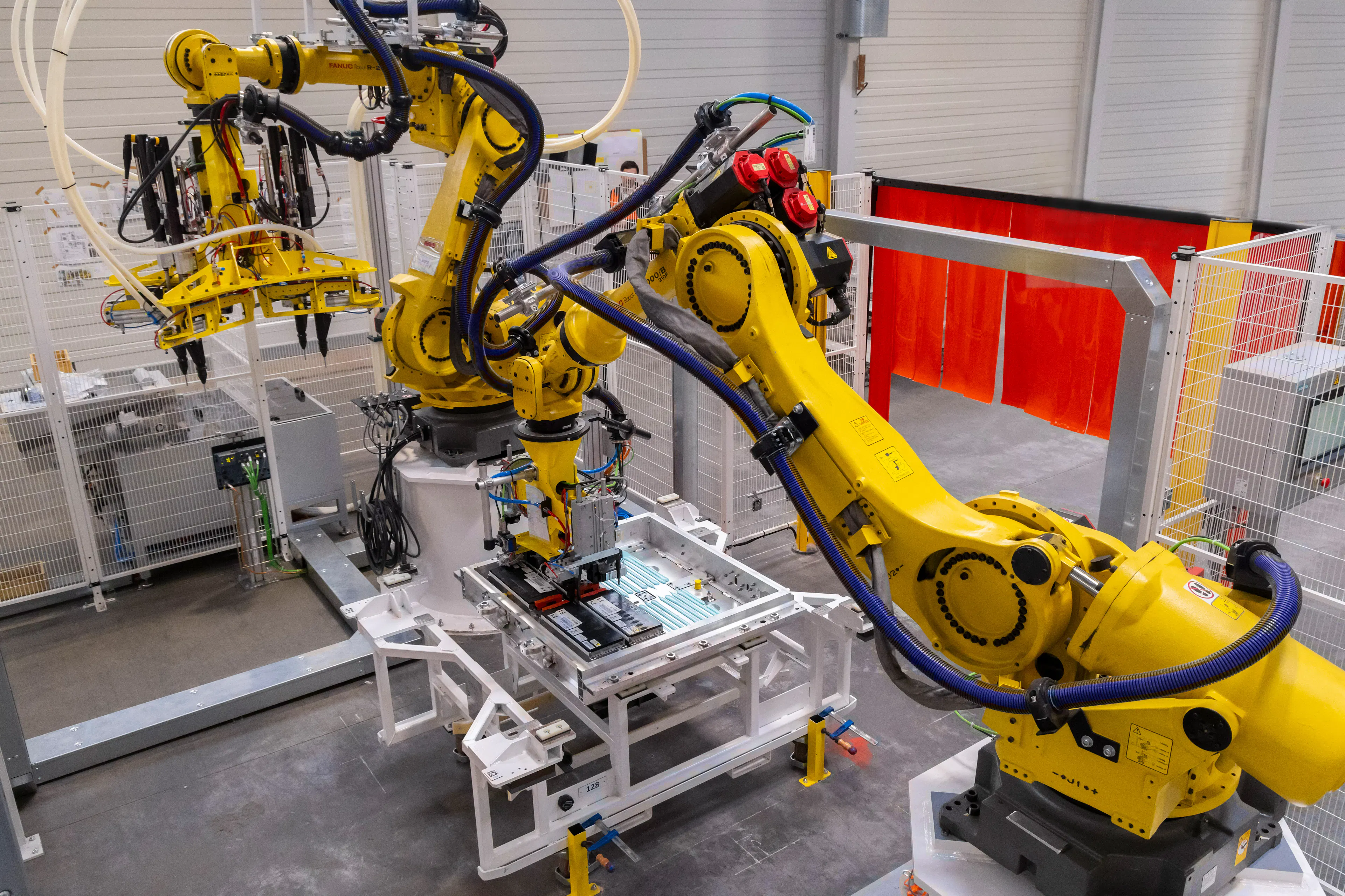 Zwei gelbe Roboterarme in einer Fabrikshalle.