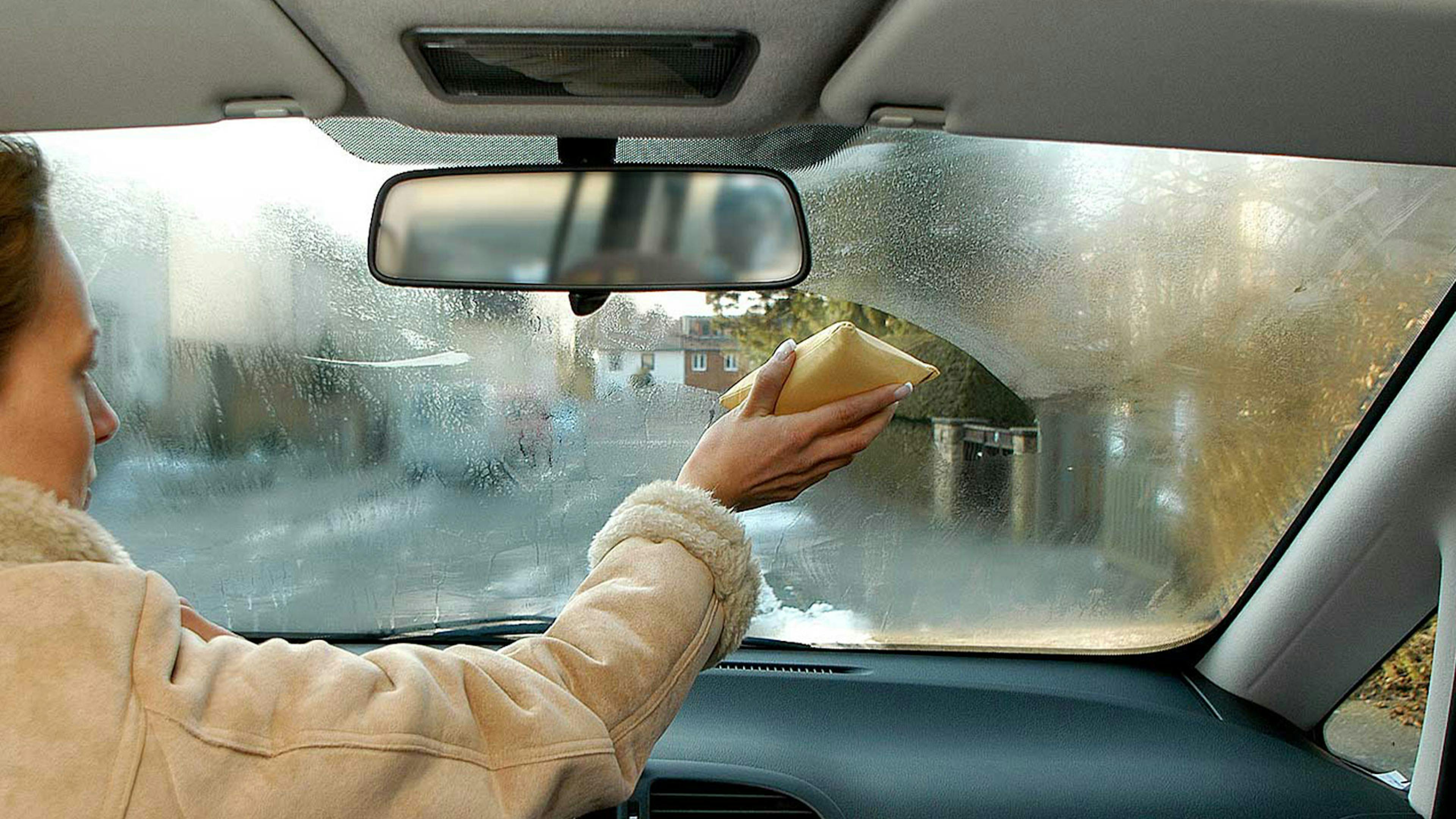 Eine Frau wischt die Windschutzscheibe ihres Autos von innen ab.