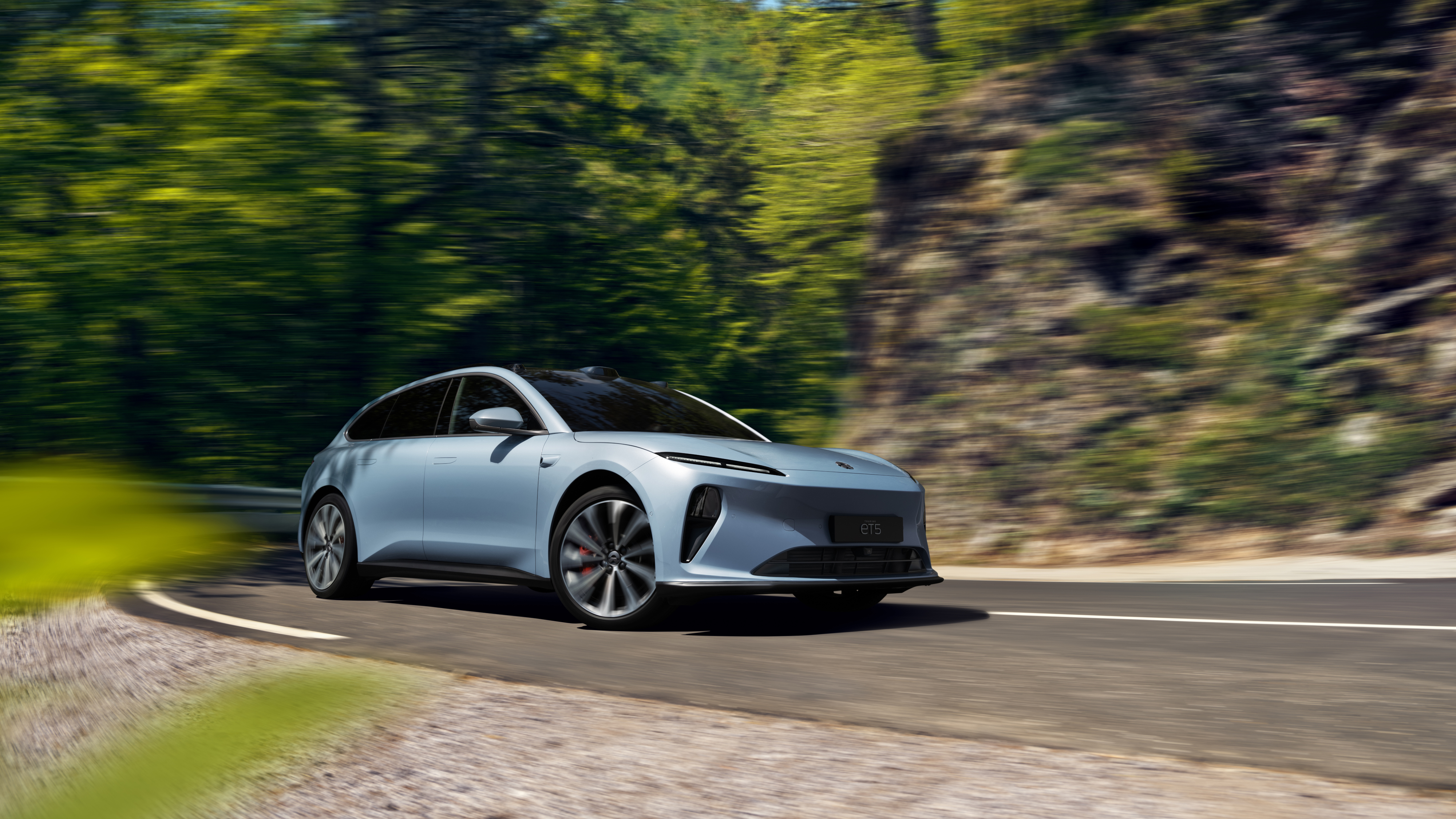 Ein hellblauer Nio ET5 Touring fährt auf einer kurvigen Bergstraße.