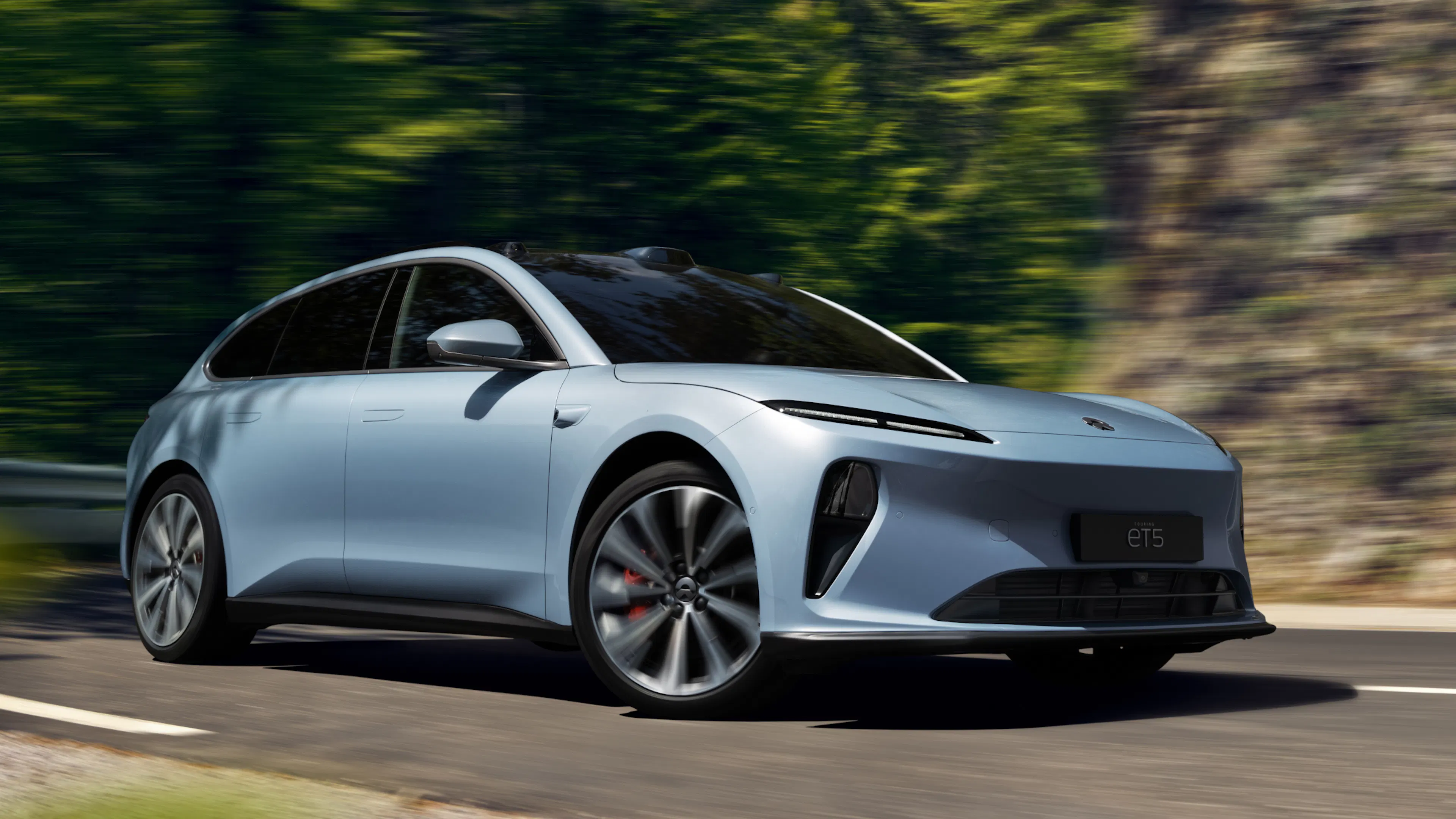 Ein hellblauer Nio ET5 Touring fährt auf einer kurvigen Bergstraße.
