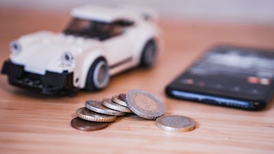 Stillleben mit einem weißen Spielzeugauto, verschiedenen Euromünzen und einem Smartphone.