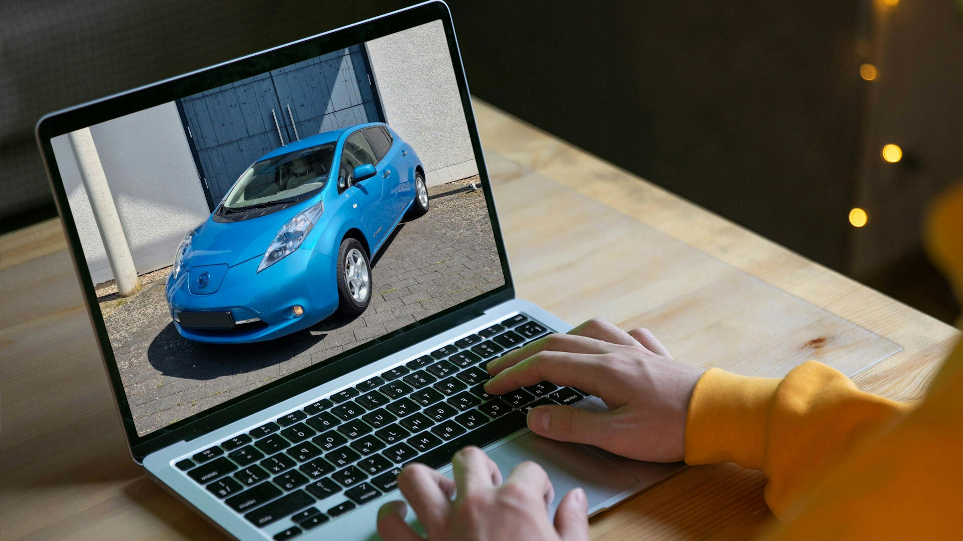 Eine Person betrachtet einen blauen Nissan Leaf der ersten Generation auf seinem Laptop-Bildschirm.