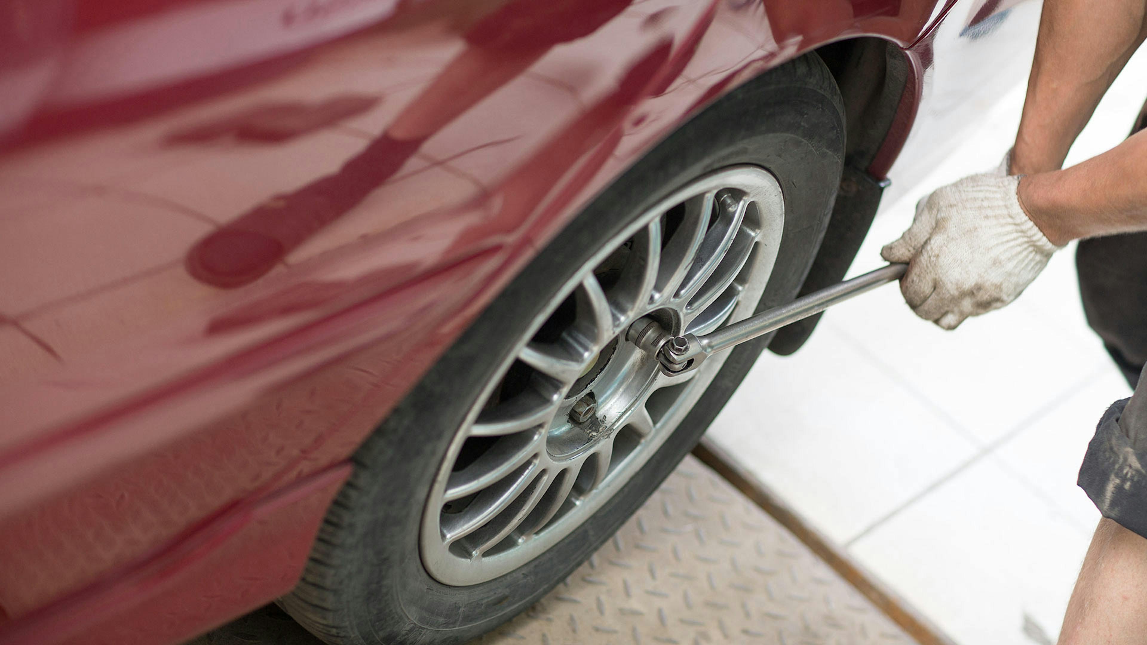 Ein Mechaniker wechselt einen Reifen an einem weinroten Pkw.