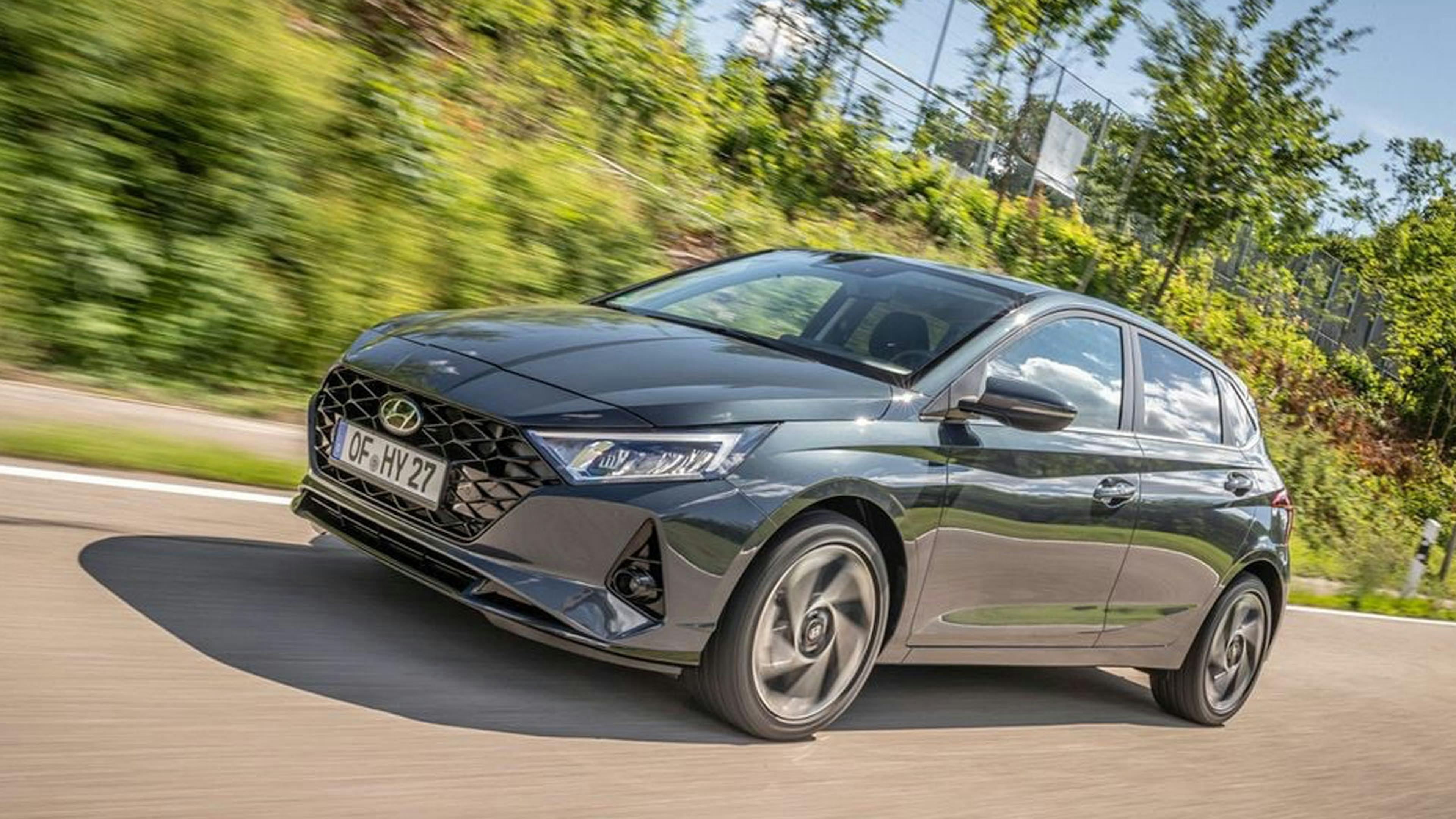 Ein grauer Hyundai i20 fährt an einer Hecke vorbei.