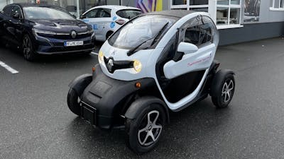 Ein schwarz-weißes Renault Twizy Microcar steht auf einem Parkplatz vor einem Autohaus.