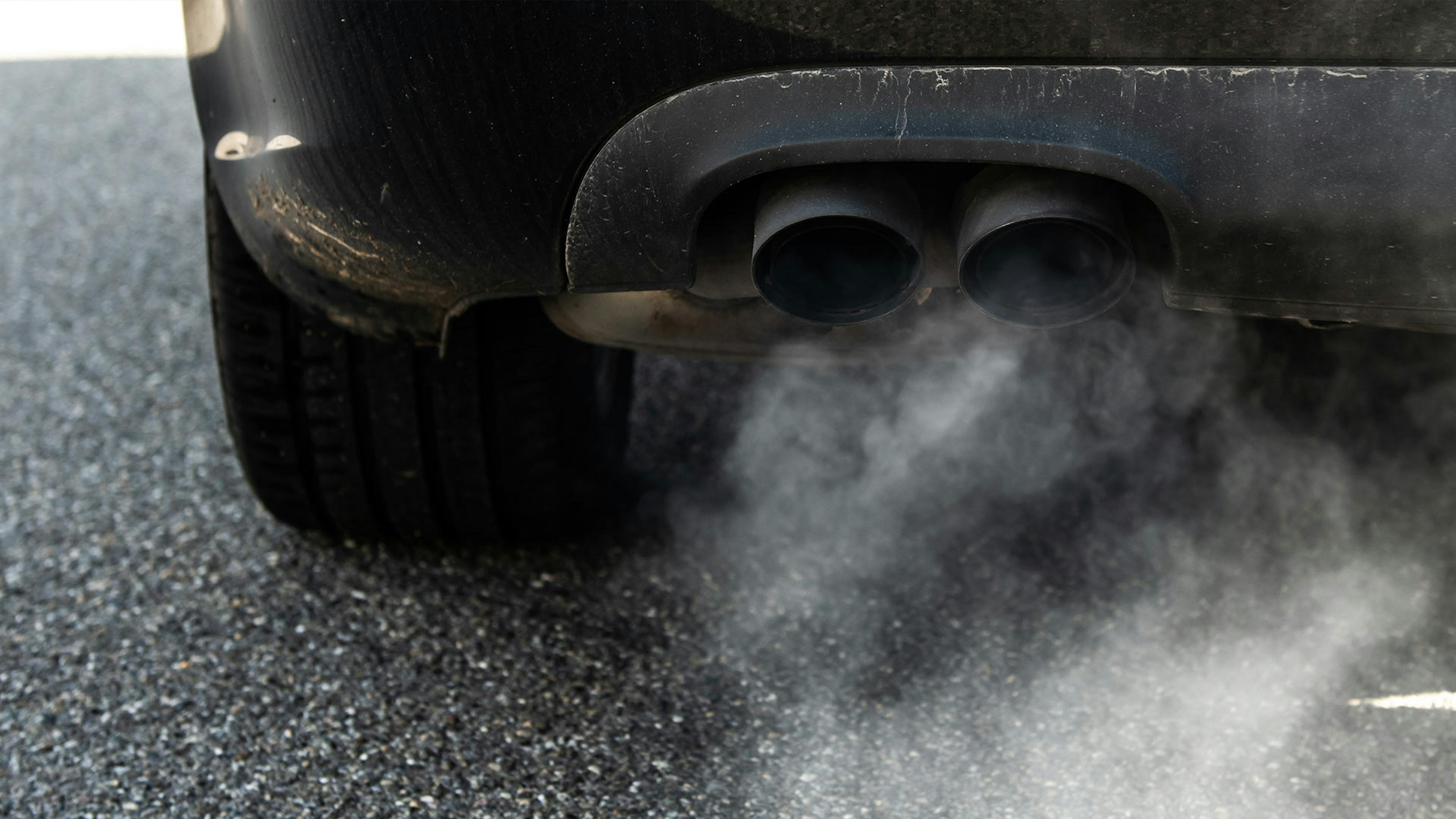 Detailaufnahme eines Pkw-Auspuffs, aus dem Abgase entweichen.