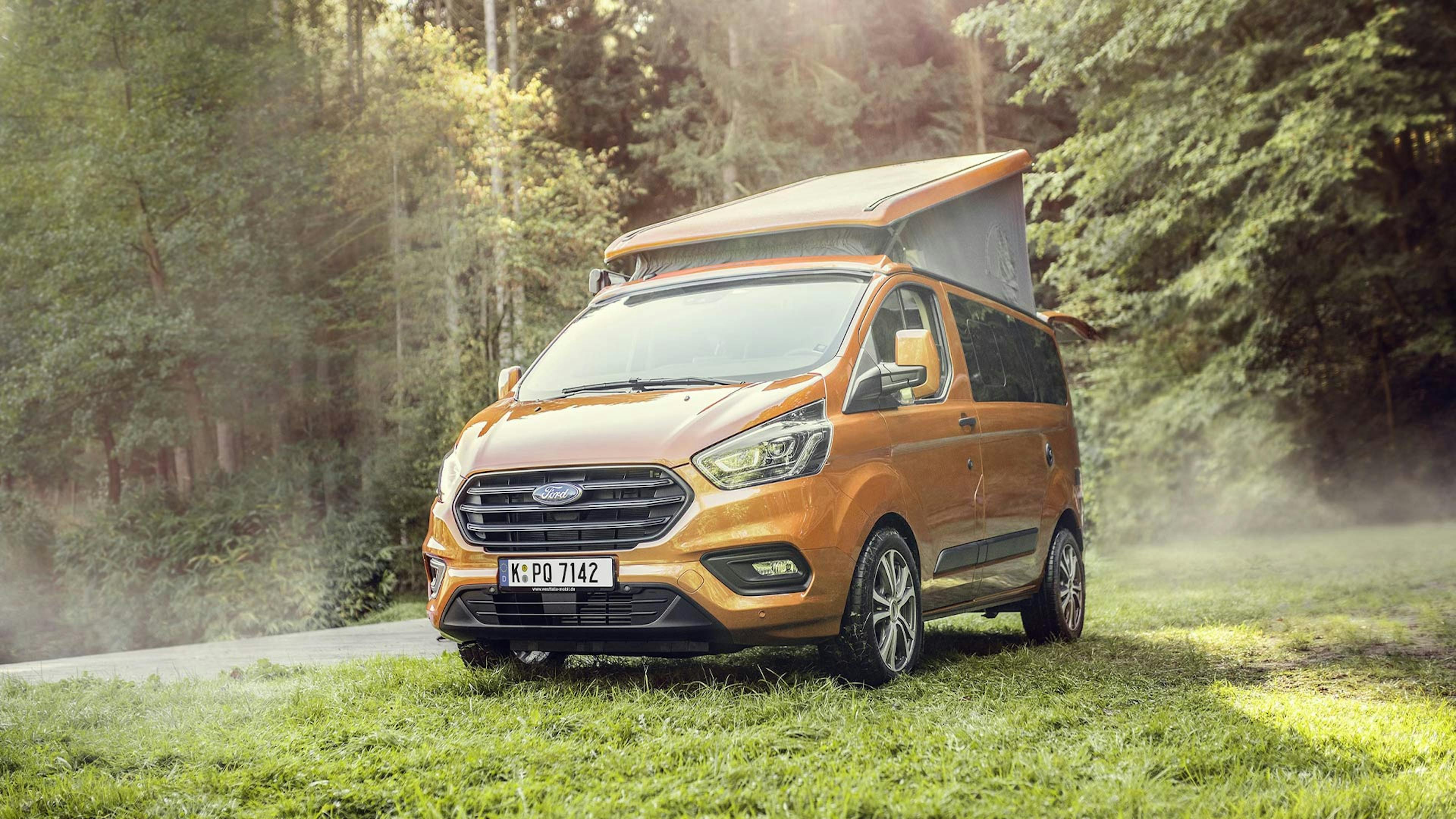 Ein goldener Ford Transit Custom Nugget Camper steht an einem Waldrand.